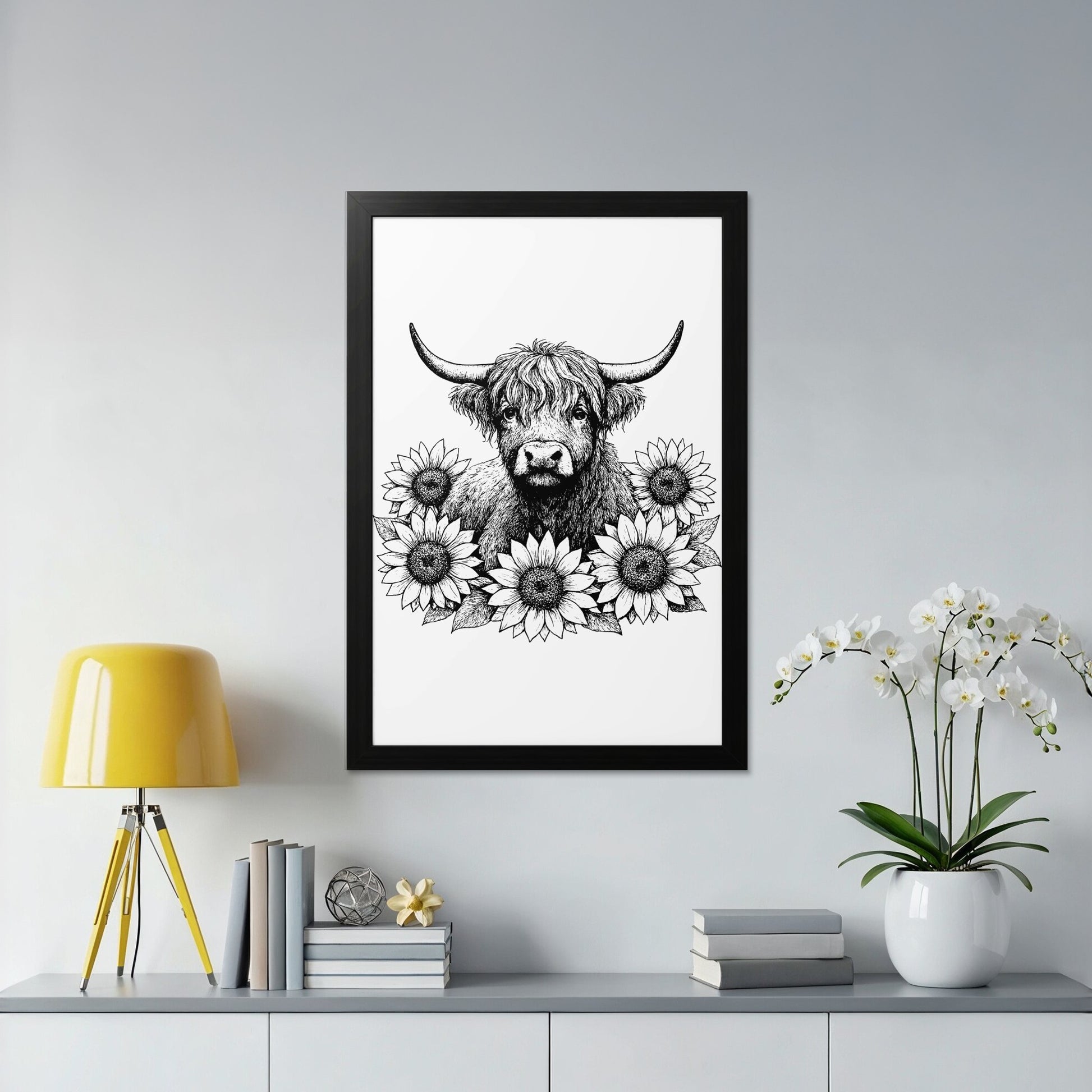 Framed artwork of a highland cow surrounded by flowers on a wall above a shelf with decor items.