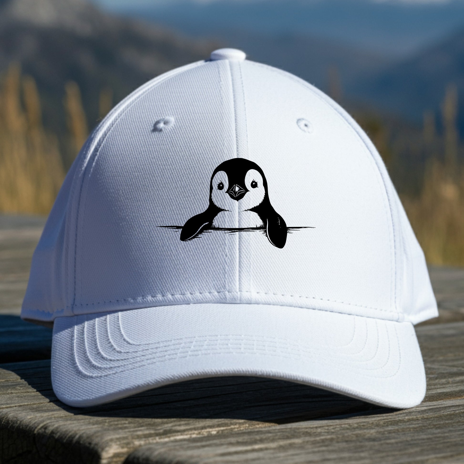 White cap with a penguin design on a wooden surface with a mountainous background