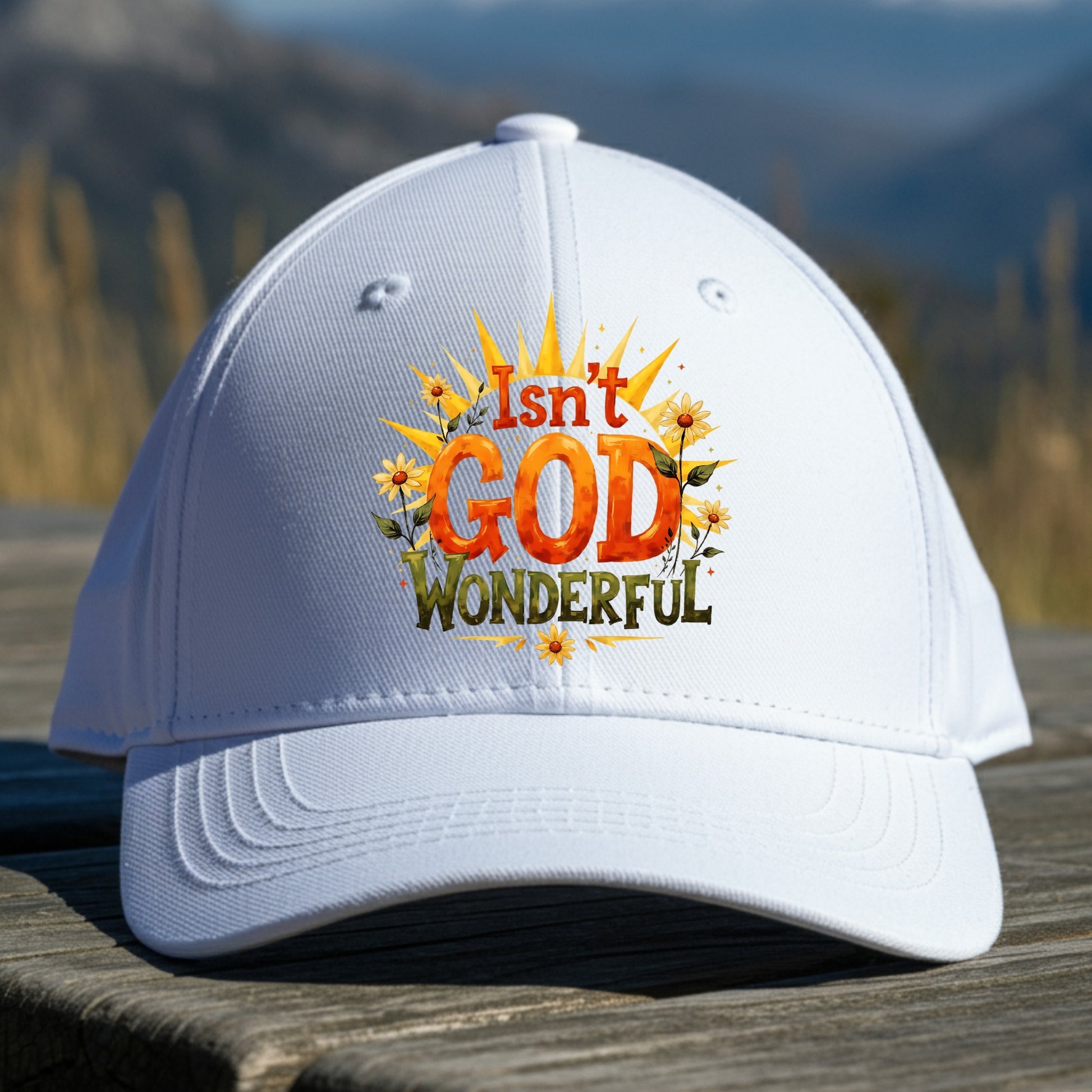 White cap with 'Isn't God Wonderful' text and sunflower design on a wooden surface with mountain background