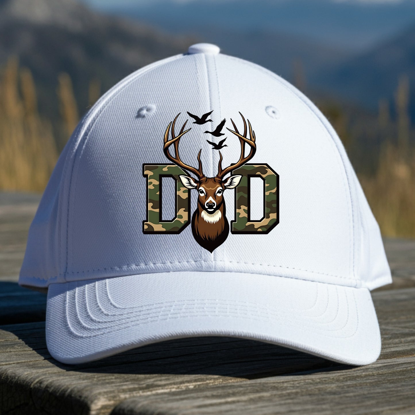 White cap with a deer and 'DAD' logo on a wooden surface with a mountain background