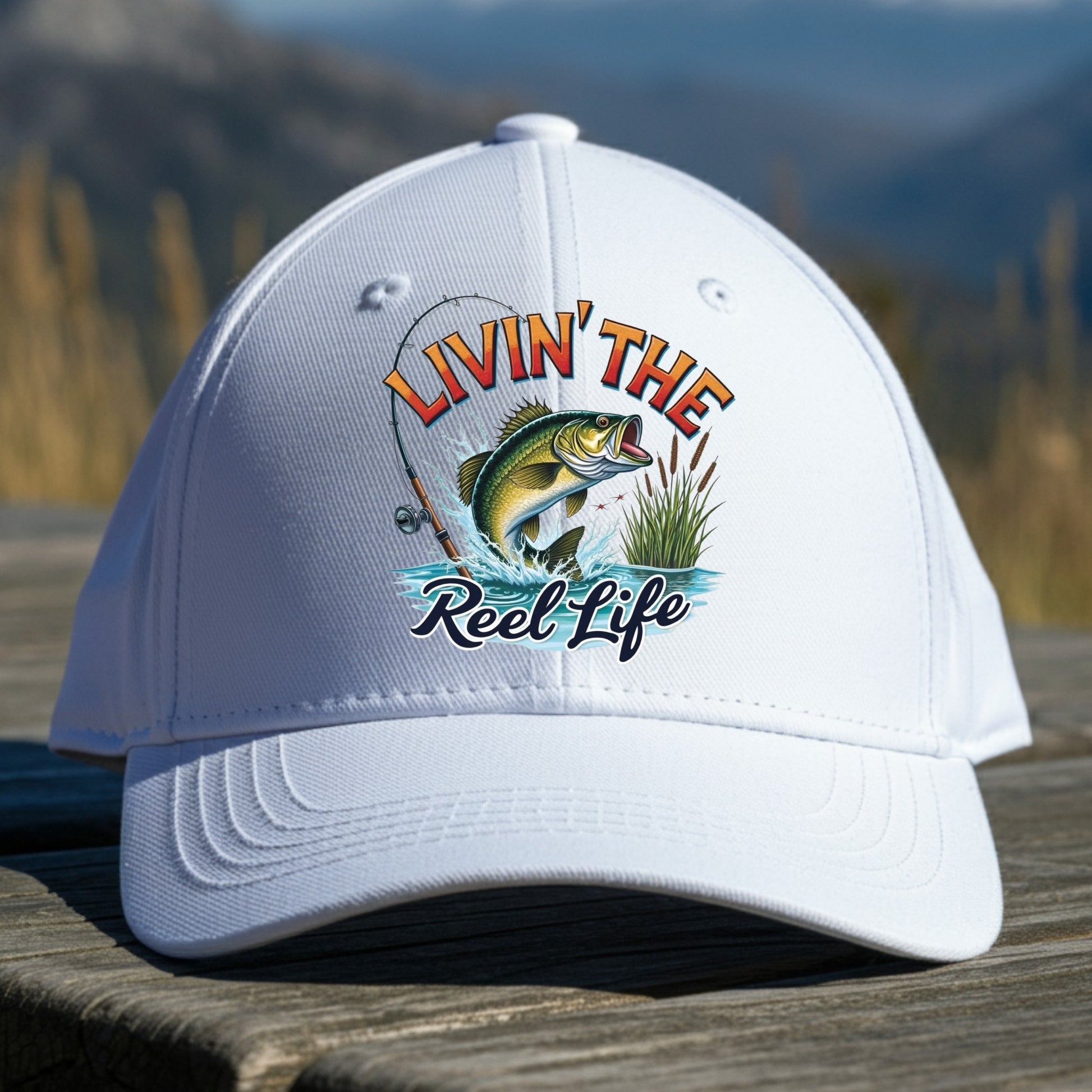White cap with 'Livin' the Reel Life' fishing graphic on a wooden surface with a natural background.