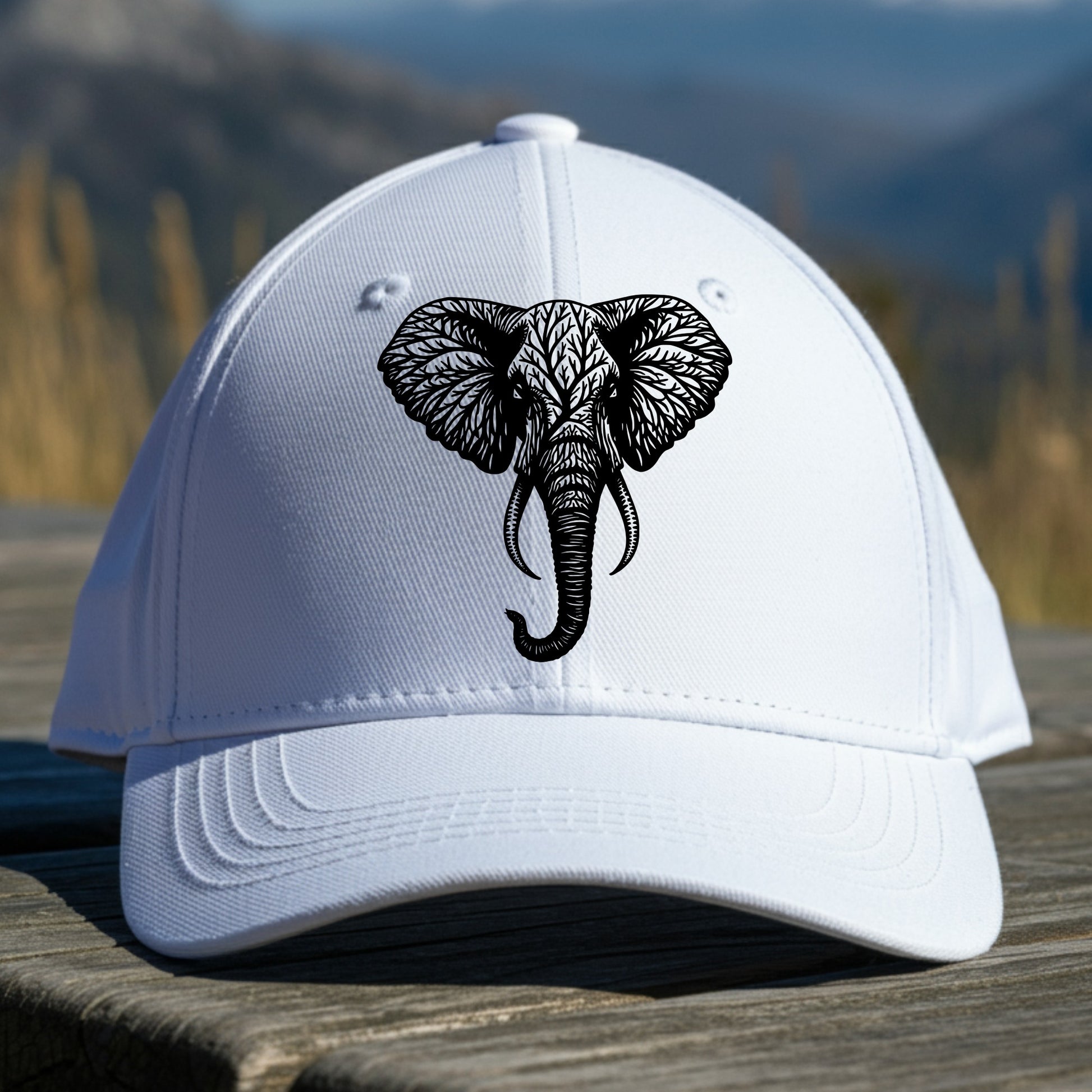 White cap with an elephant design sitting on a wooden surface with a mountainous background