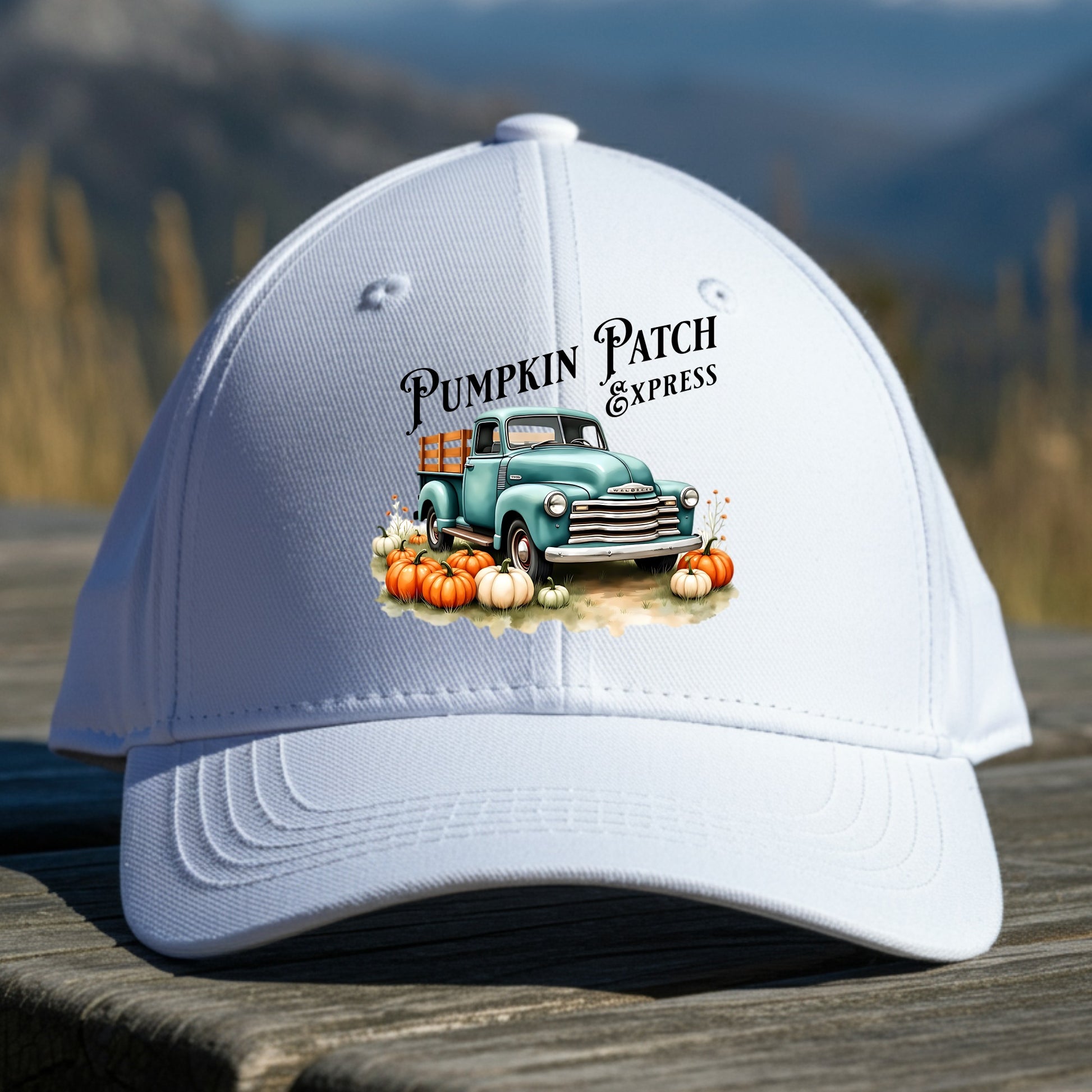 White cap with 'Pumpkin Patch Express' design featuring a truck and pumpkins on a wooden surface with a mountain background.