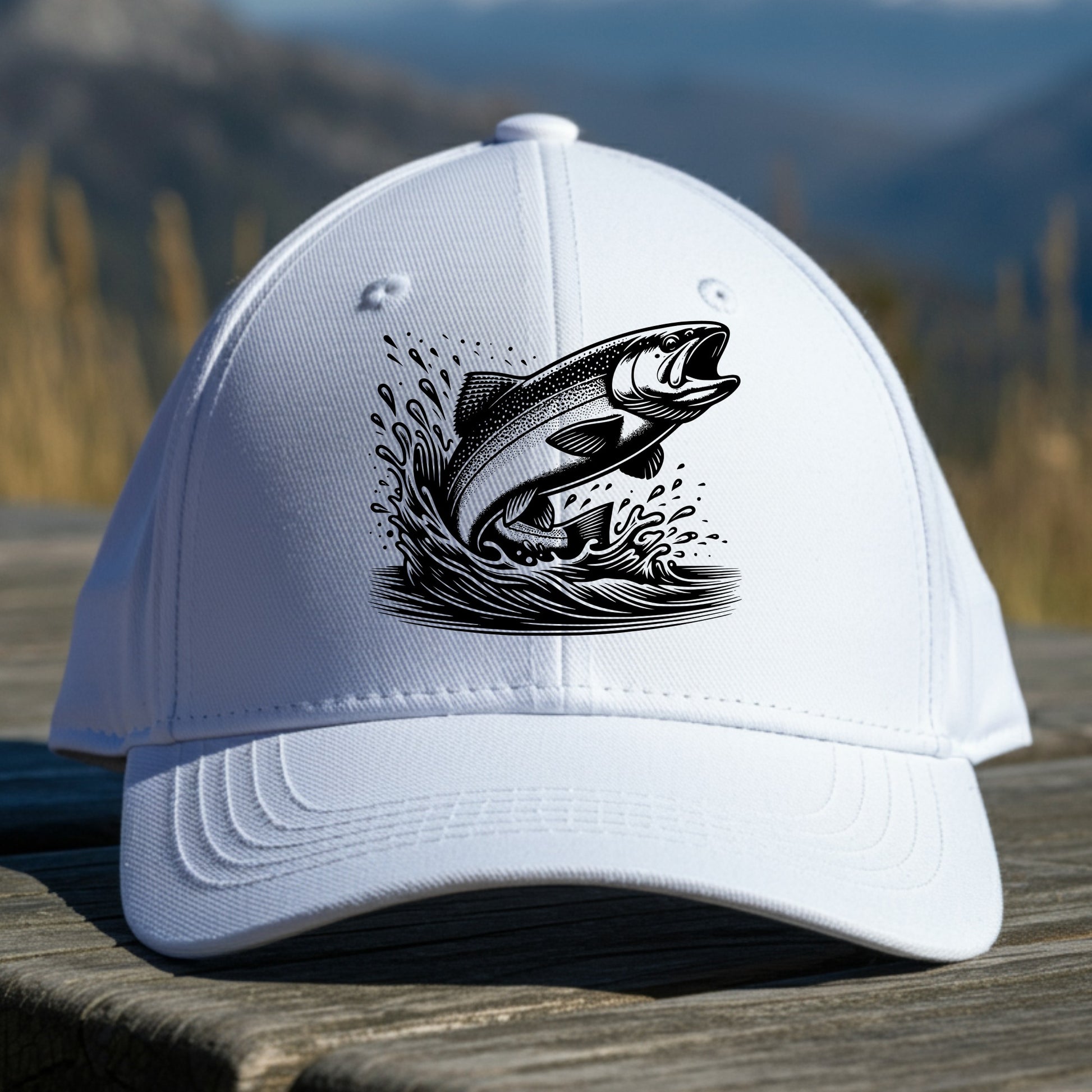 White cap with a black trout fish design on a wooden surface with a mountain background
