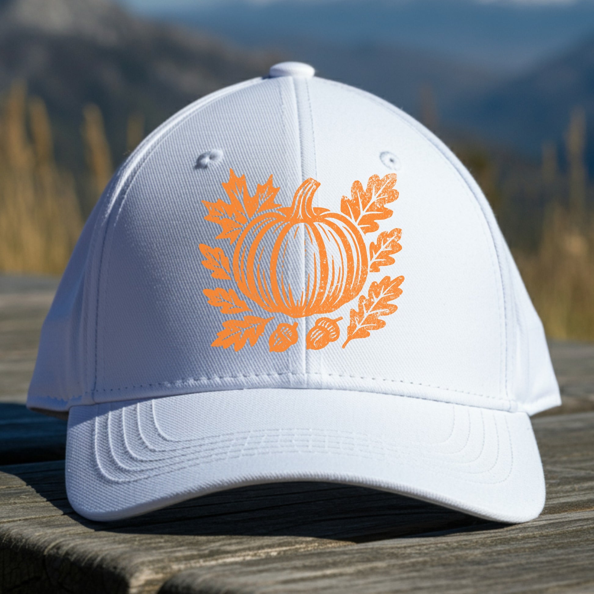 White cap with orange pumpkin design on a wooden surface with a mountain background