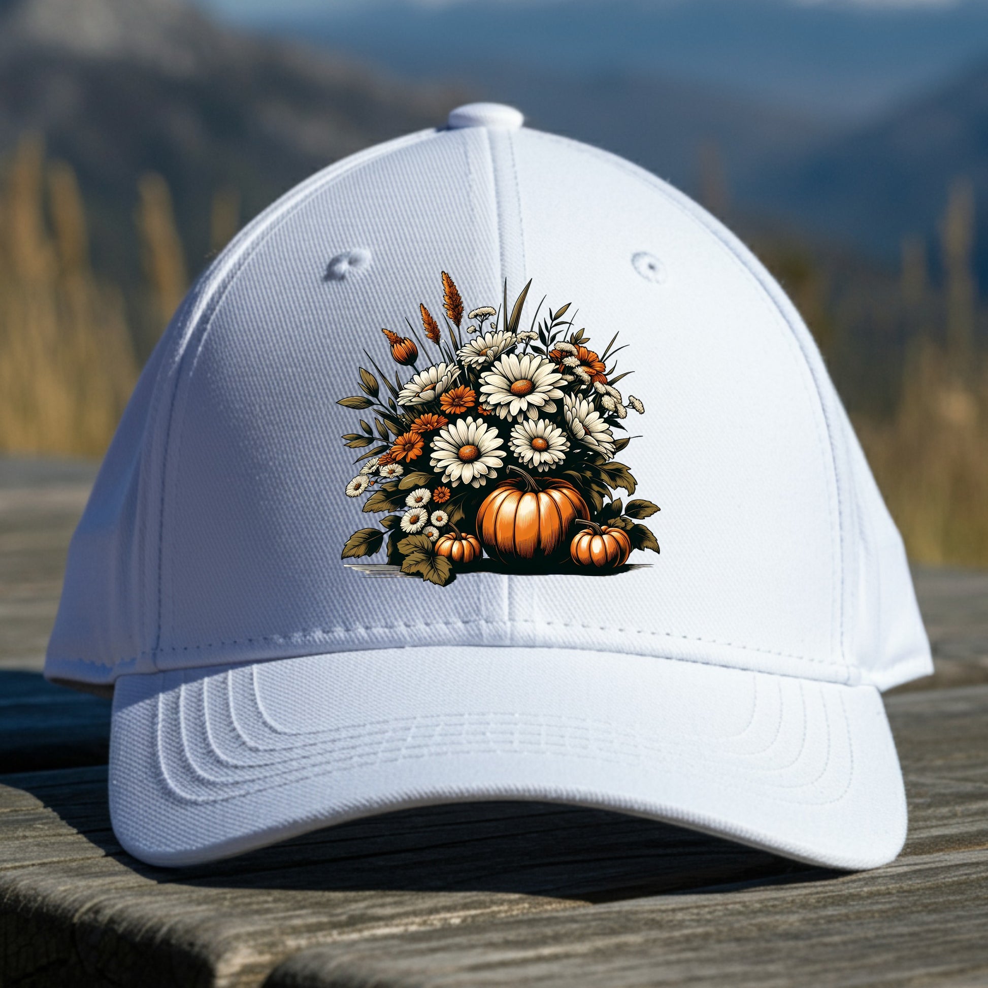 White cap with autumn-themed design featuring pumpkins and flowers on a wooden surface with a mountain background.