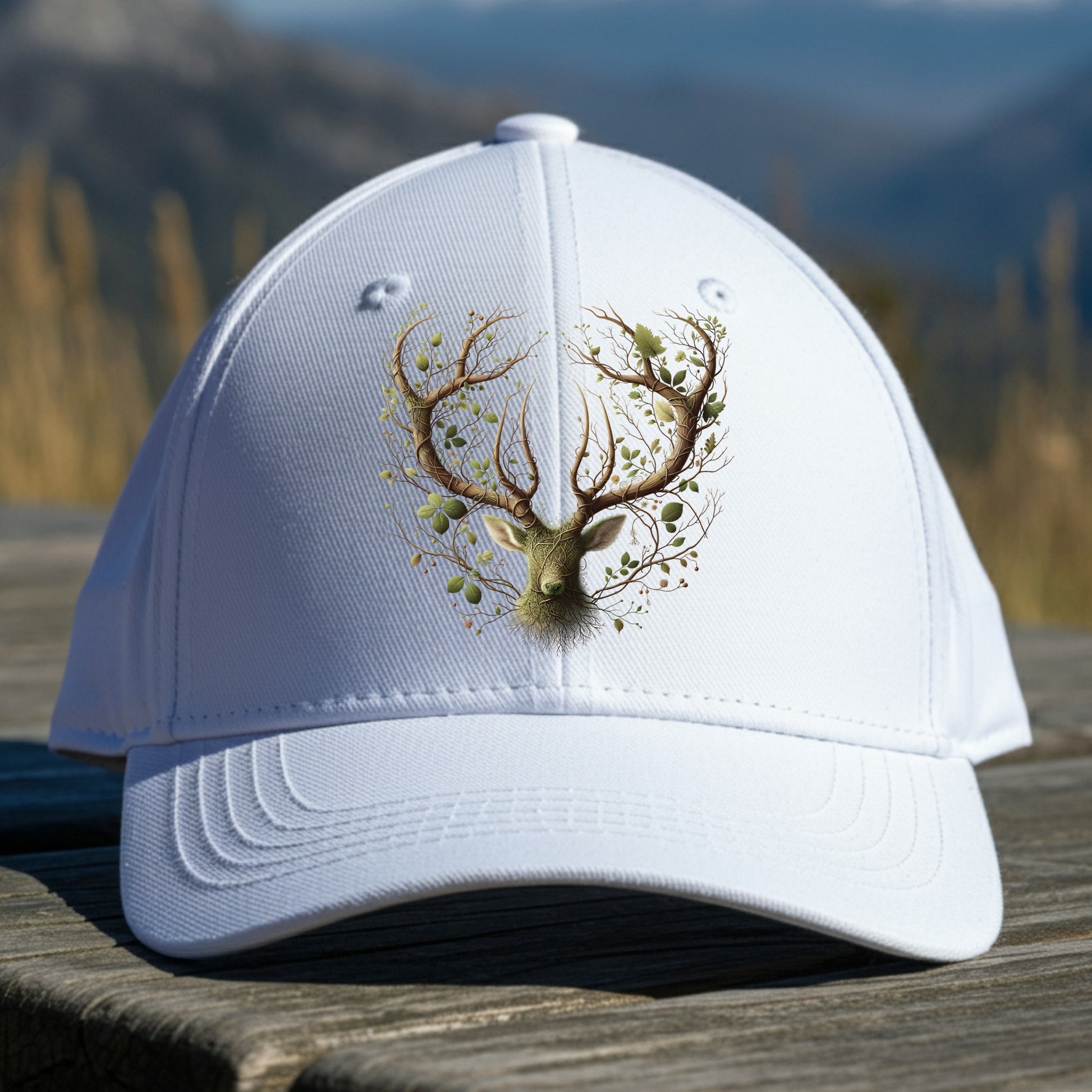 White cap with deer and foliage design on a wooden surface with a mountainous background