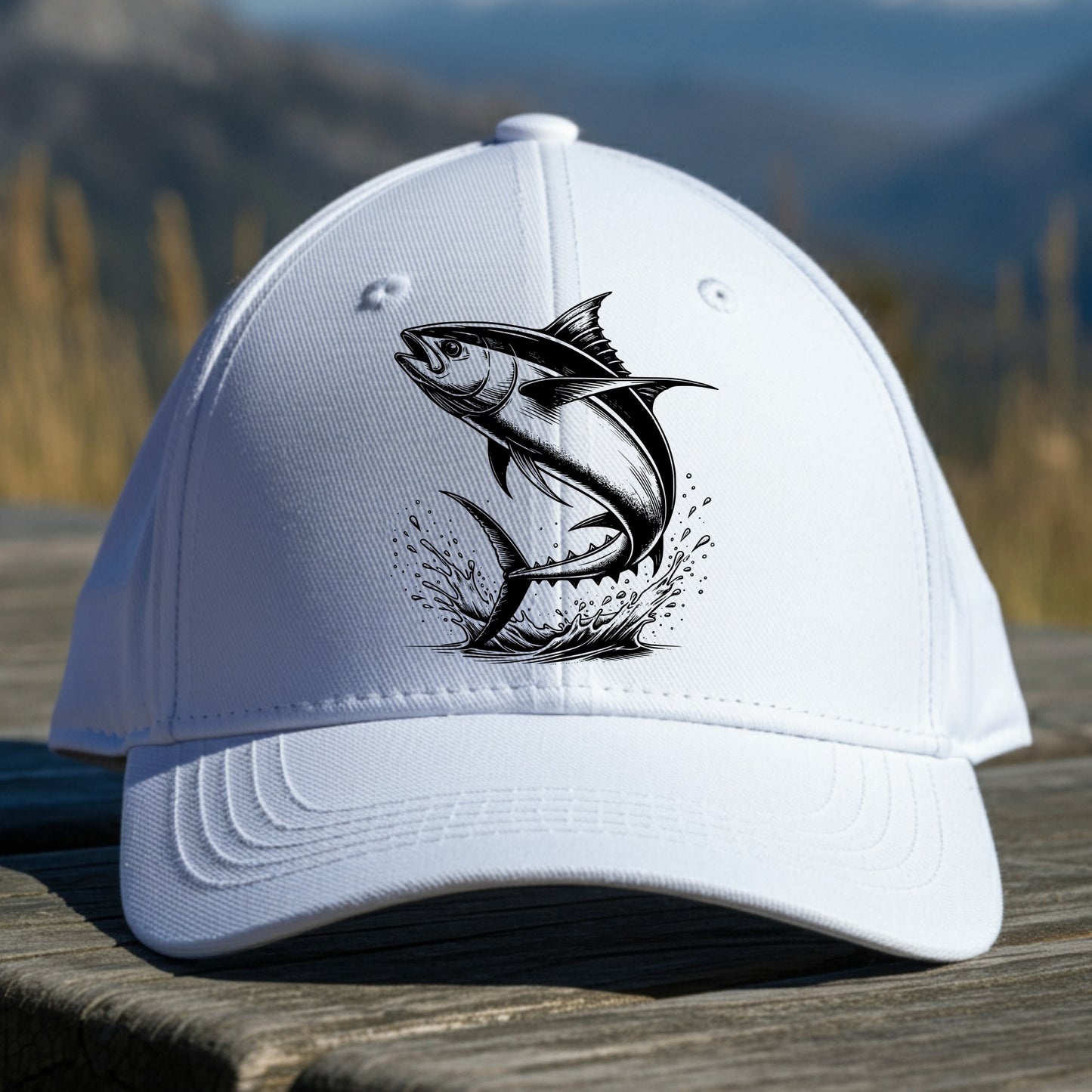White cap with a black tuna fish design on a wooden surface with a mountainous background