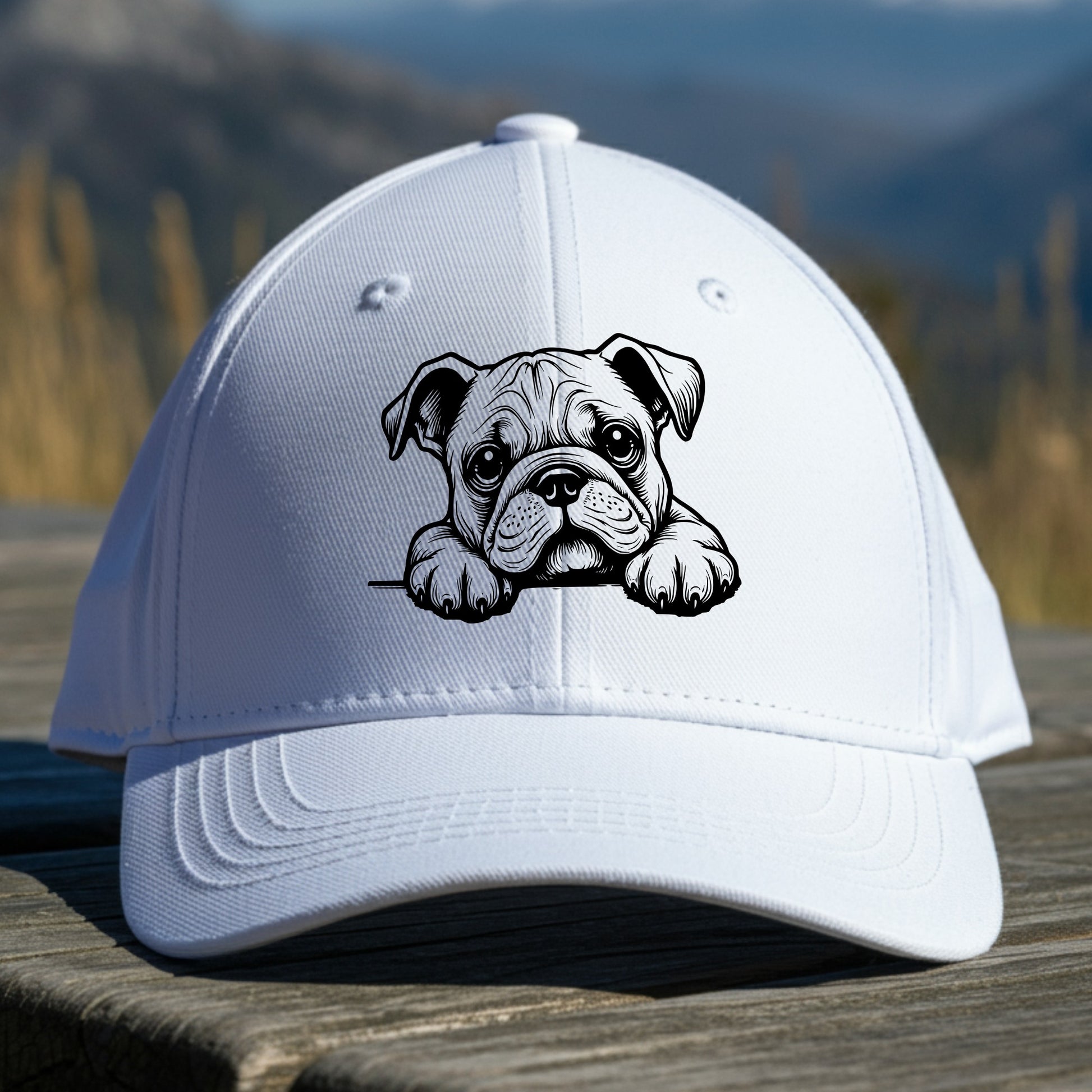 White cap with a bulldog illustration sitting on a wooden surface with a mountainous background