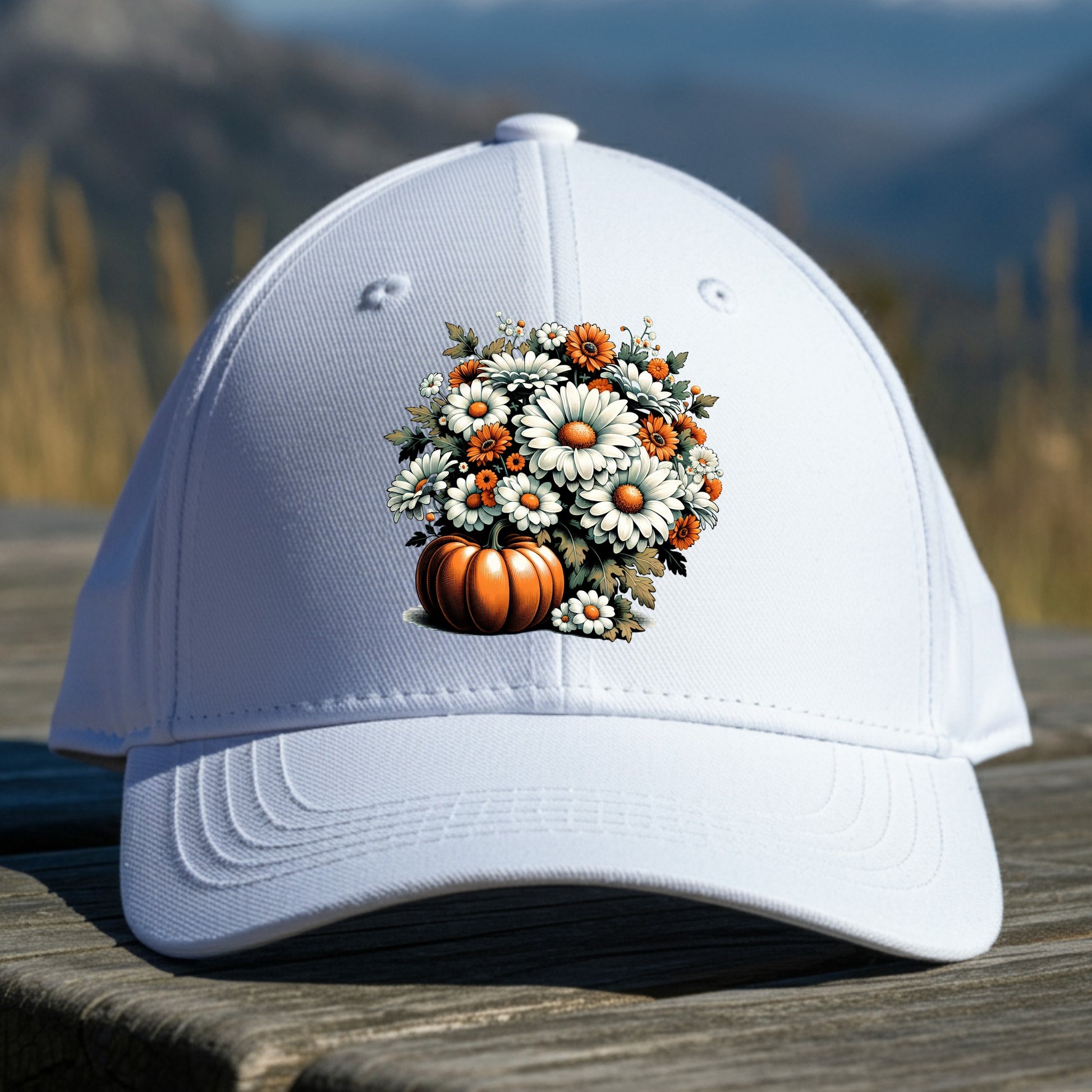 White cap with a pumpkin and floral design on a wooden surface with a mountainous background