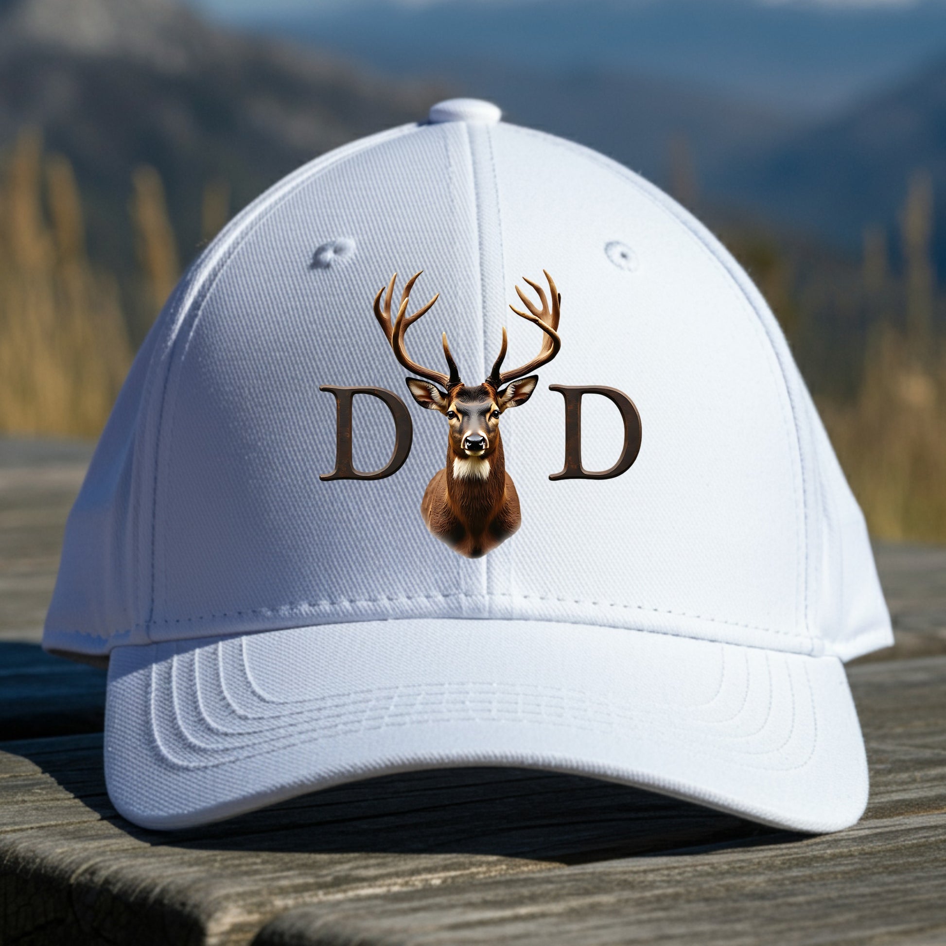 White cap with deer design and 'DAD' text on a wooden surface with a mountain background