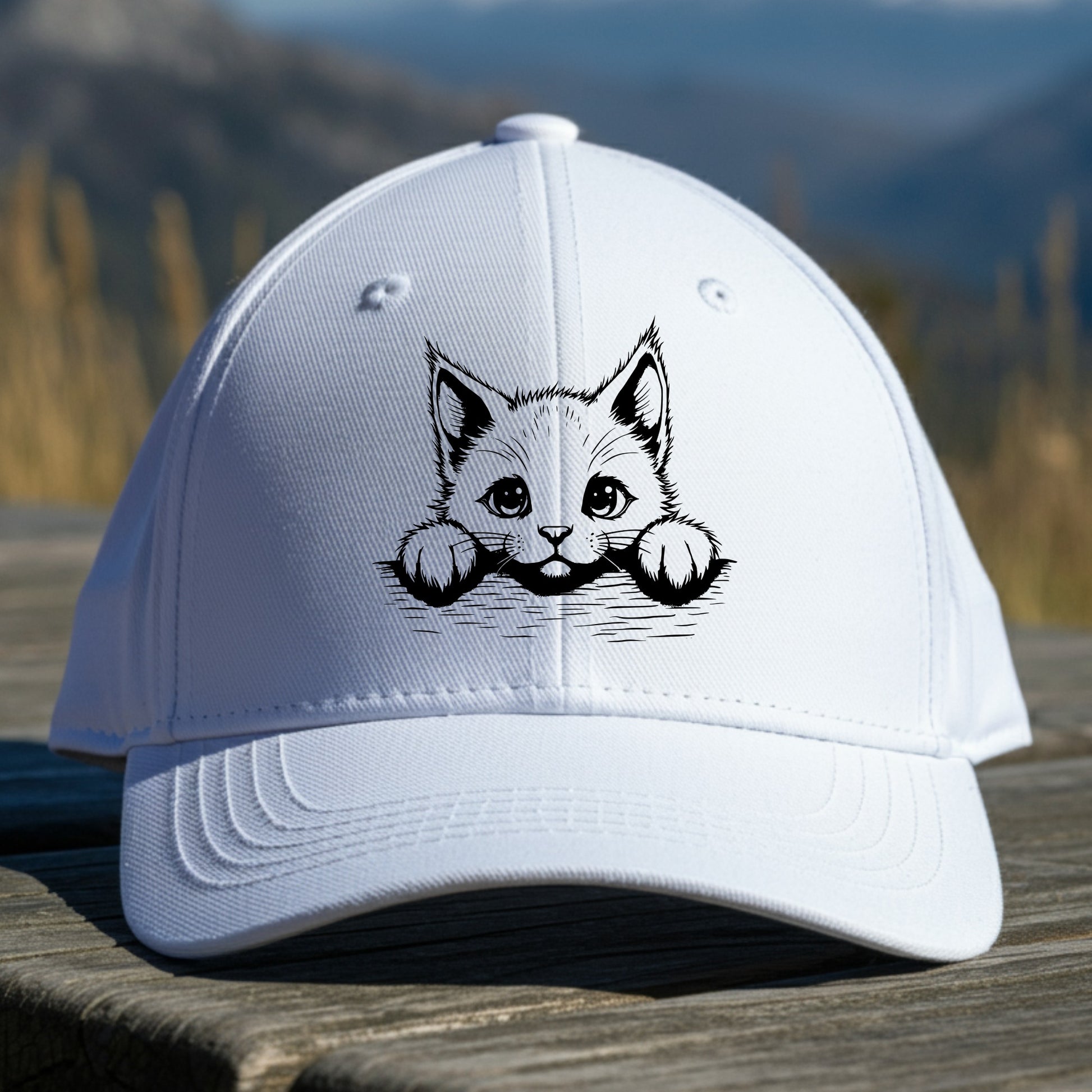 White cap with a cat illustration on a wooden surface with a mountain background
