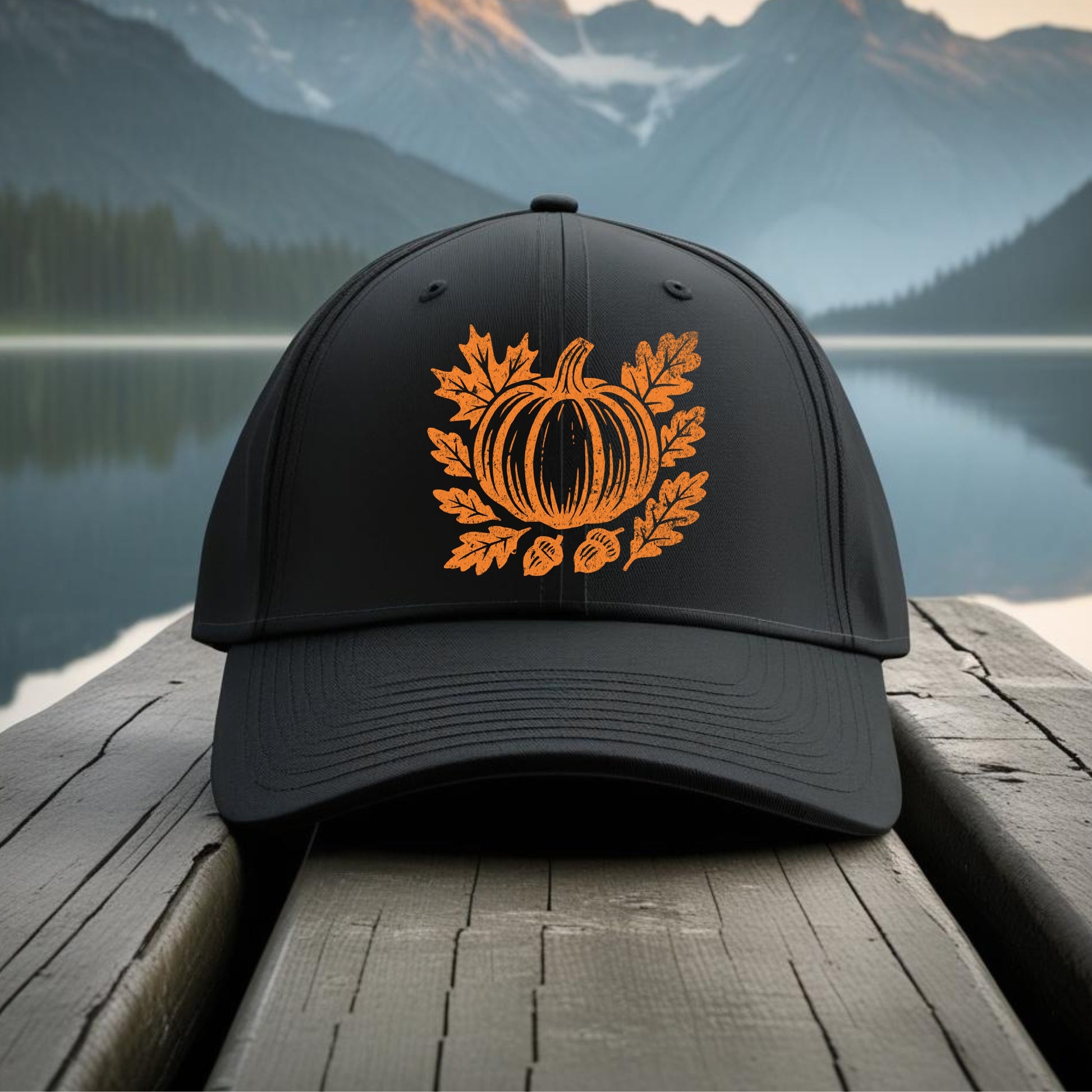 Black cap with orange pumpkin design on a wooden dock with a mountain and lake background