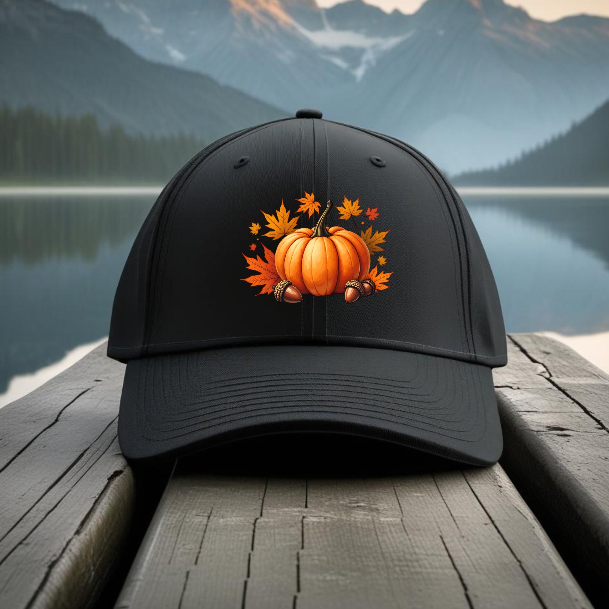 Black cap with pumpkin and leaf design on a wooden dock with mountain and lake background