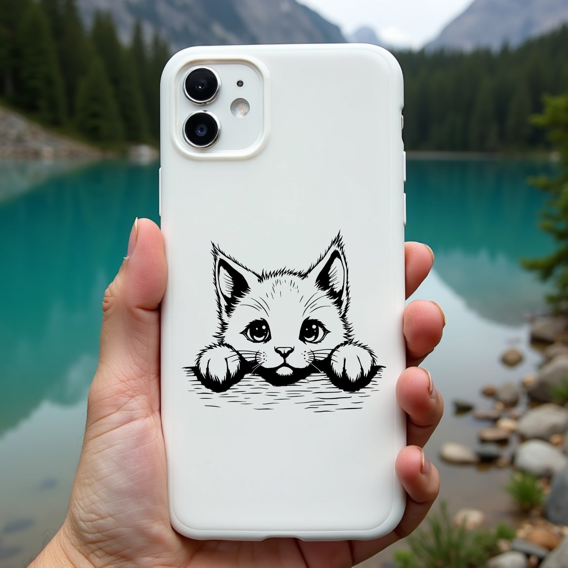 Phone case with a cat design held by a hand against a scenic background of a lake and mountains.