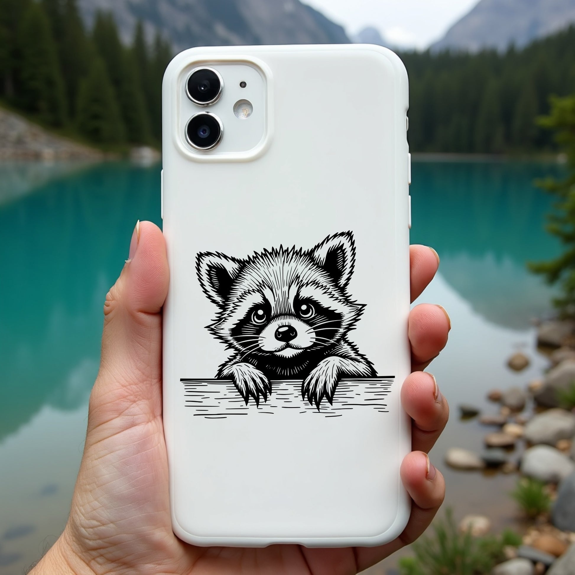 Phone case with raccoon design held in front of a scenic lake and mountains