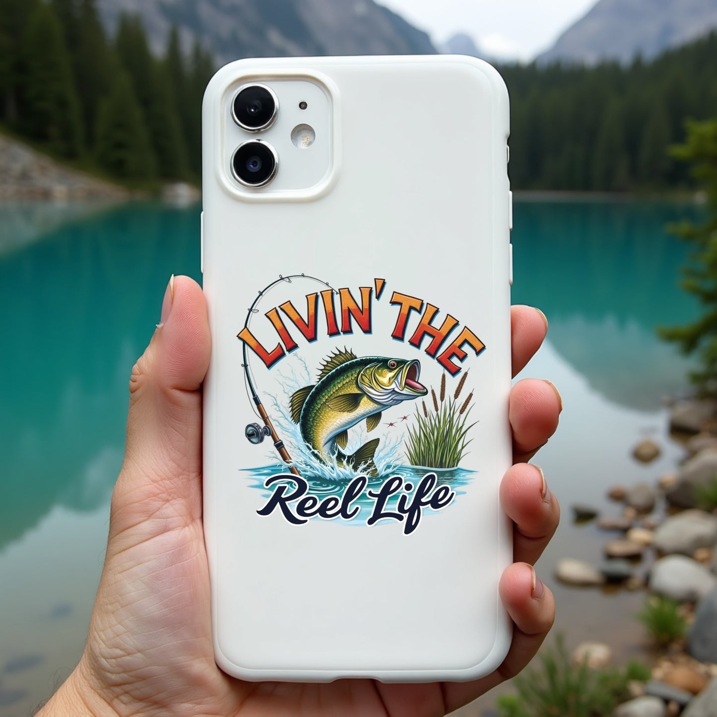 Phone case with 'Livin' the Reel Life' design held in front of a scenic lake.