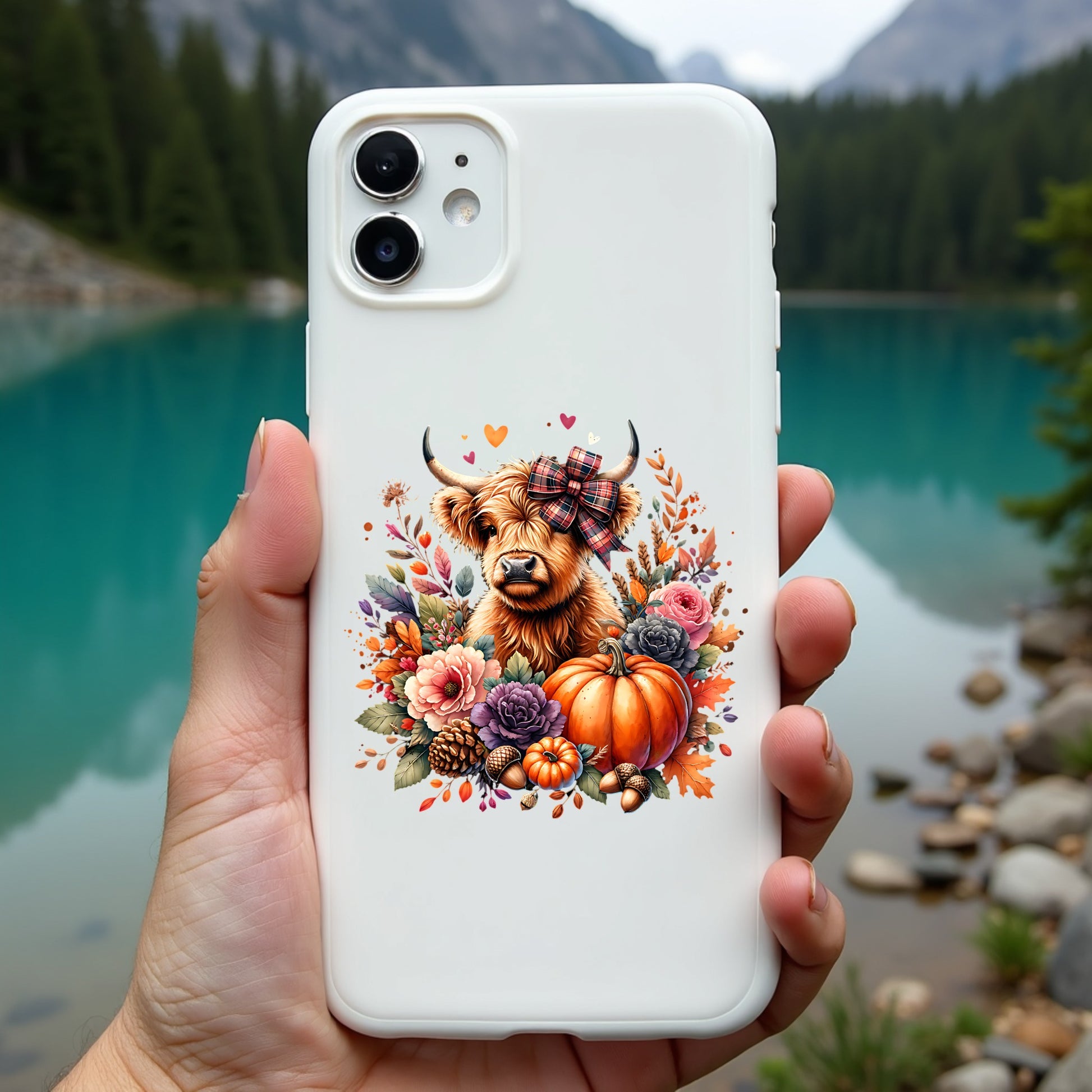 Phone case with a highland cow and autumn elements held in front of a scenic lake.
