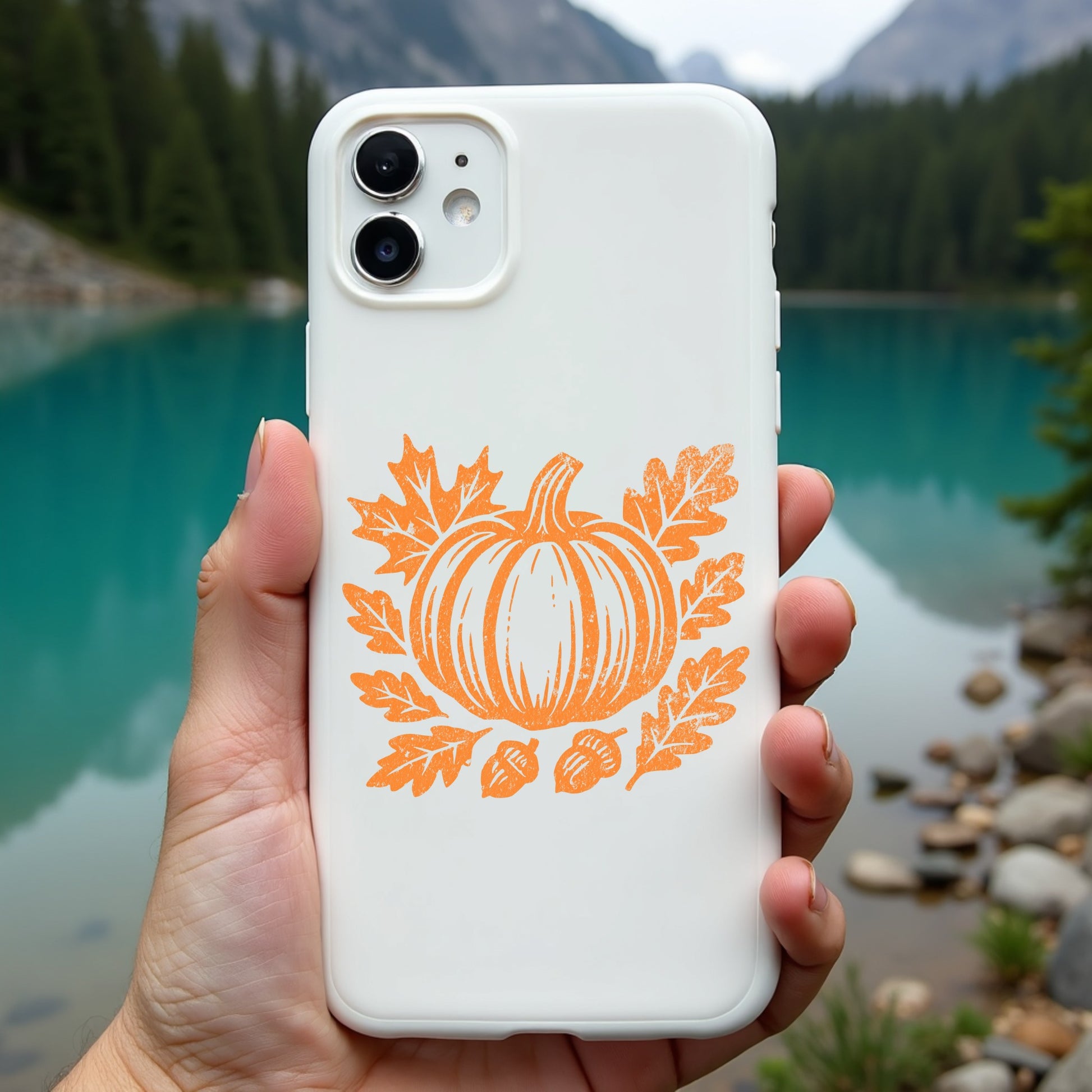 Phone case with pumpkin design held in front of a scenic lake and mountains