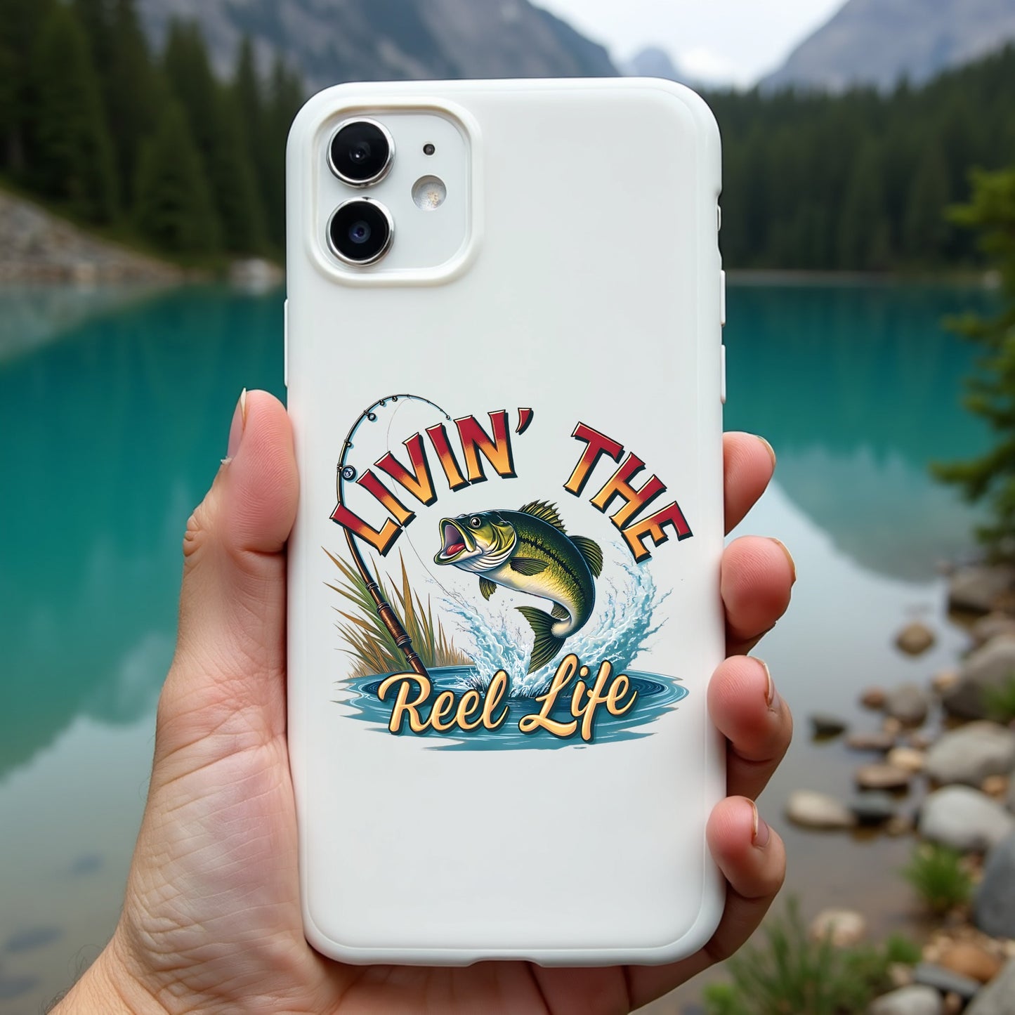 Phone case with 'Livin' the Reel Life' design held in front of a scenic lake.