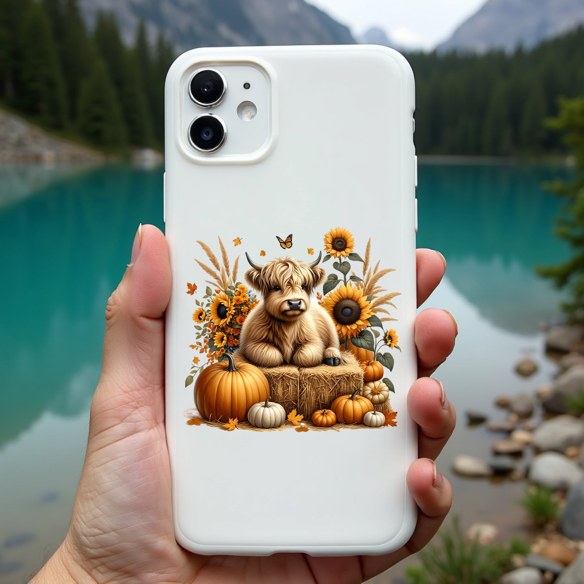 Phone case with a highland cow and autumn design held in front of a scenic lake.