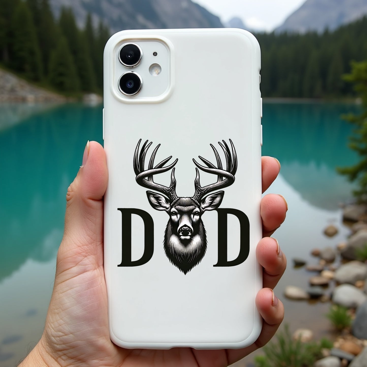 Phone case with deer design and 'DAD' text held in front of a scenic lake and mountains.