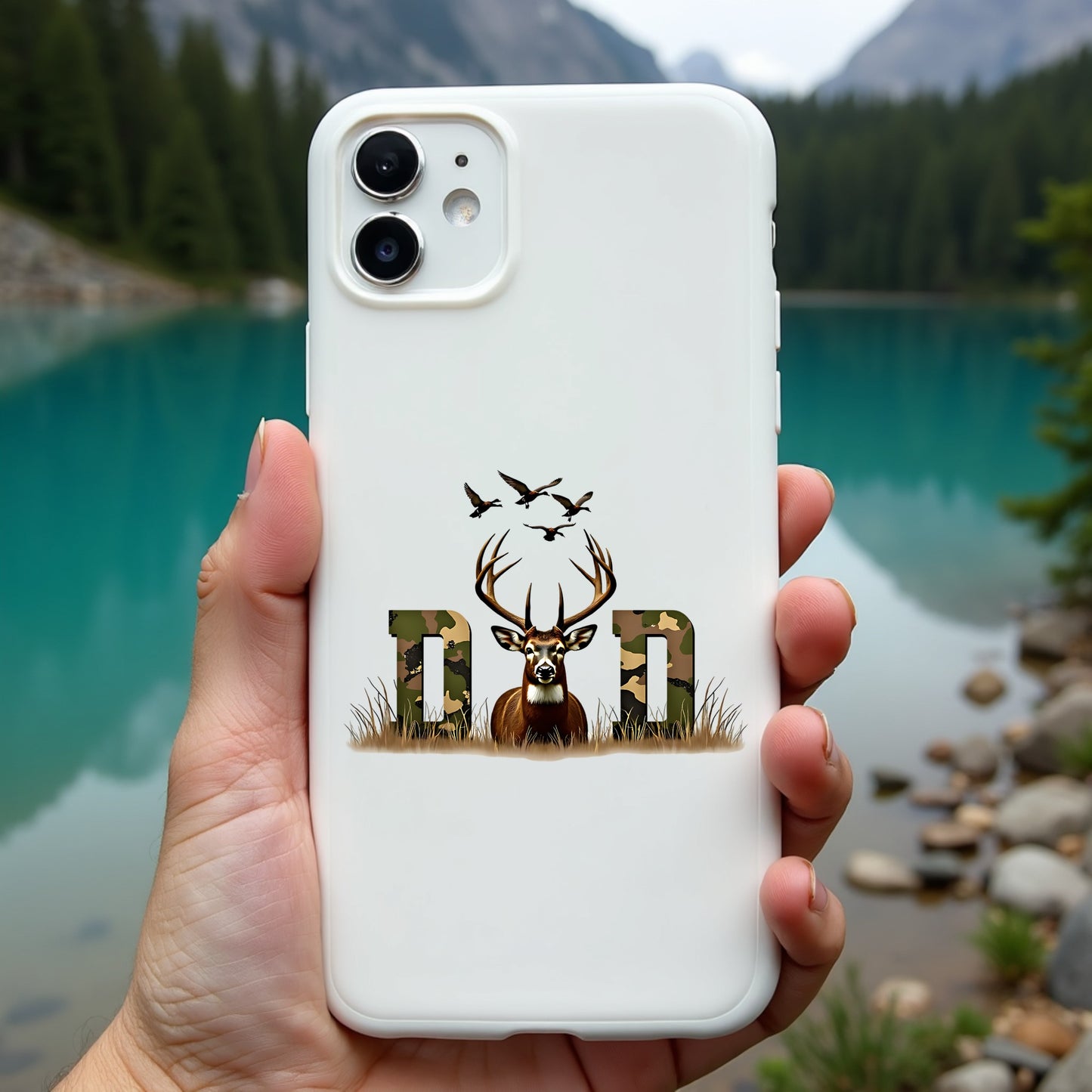 Phone case with deer design and 'Dad' text held in front of a scenic lake and mountains.