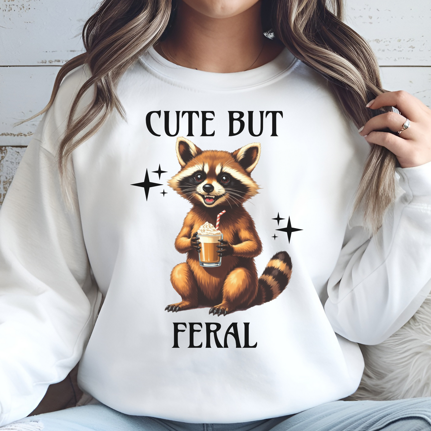 Cute But Feral raccoon holding a latte digital design on a woman's white sweatshirt