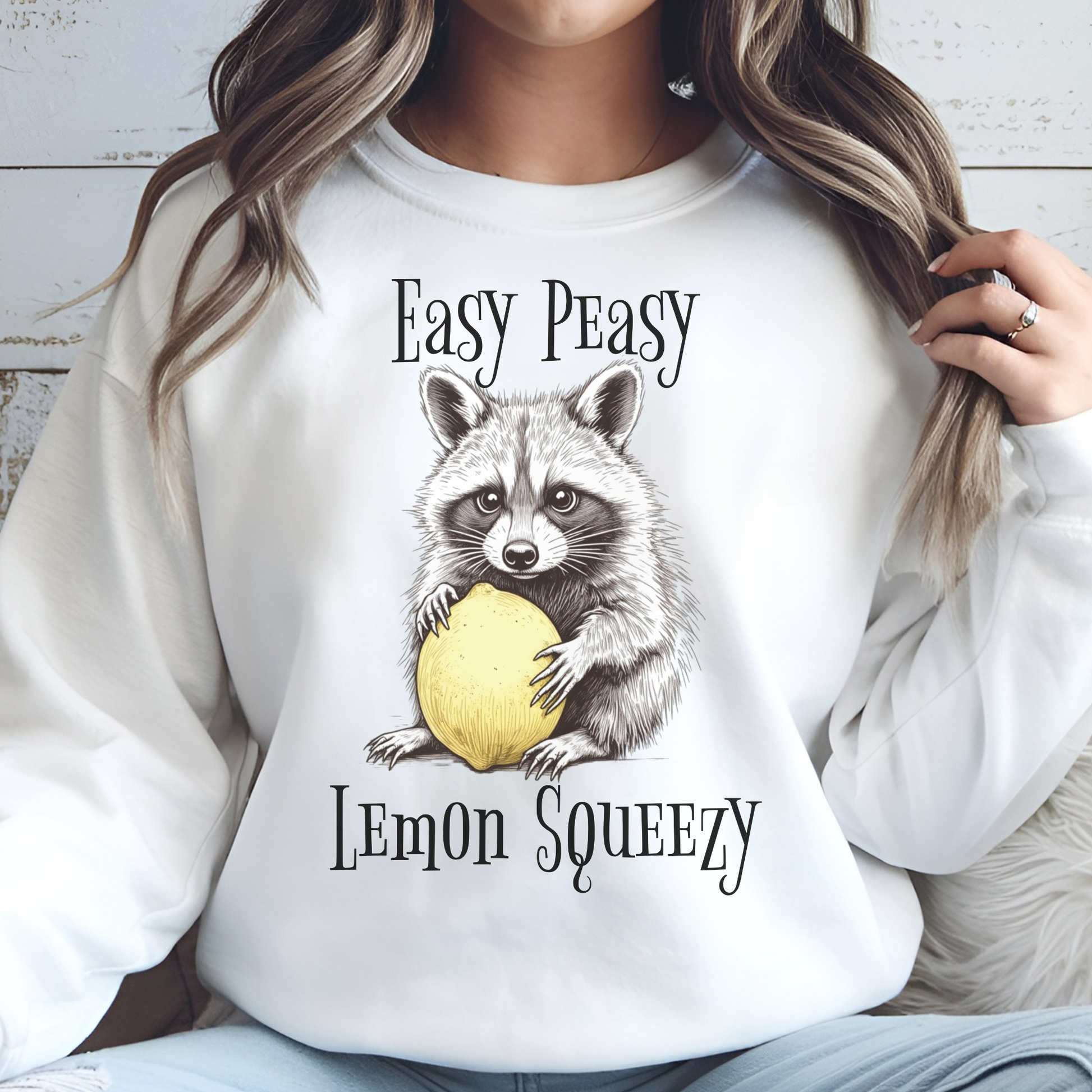 Easy Peasy Lemon Squeezy raccoon holding a lemon digital design on a woman's white sweatshirt