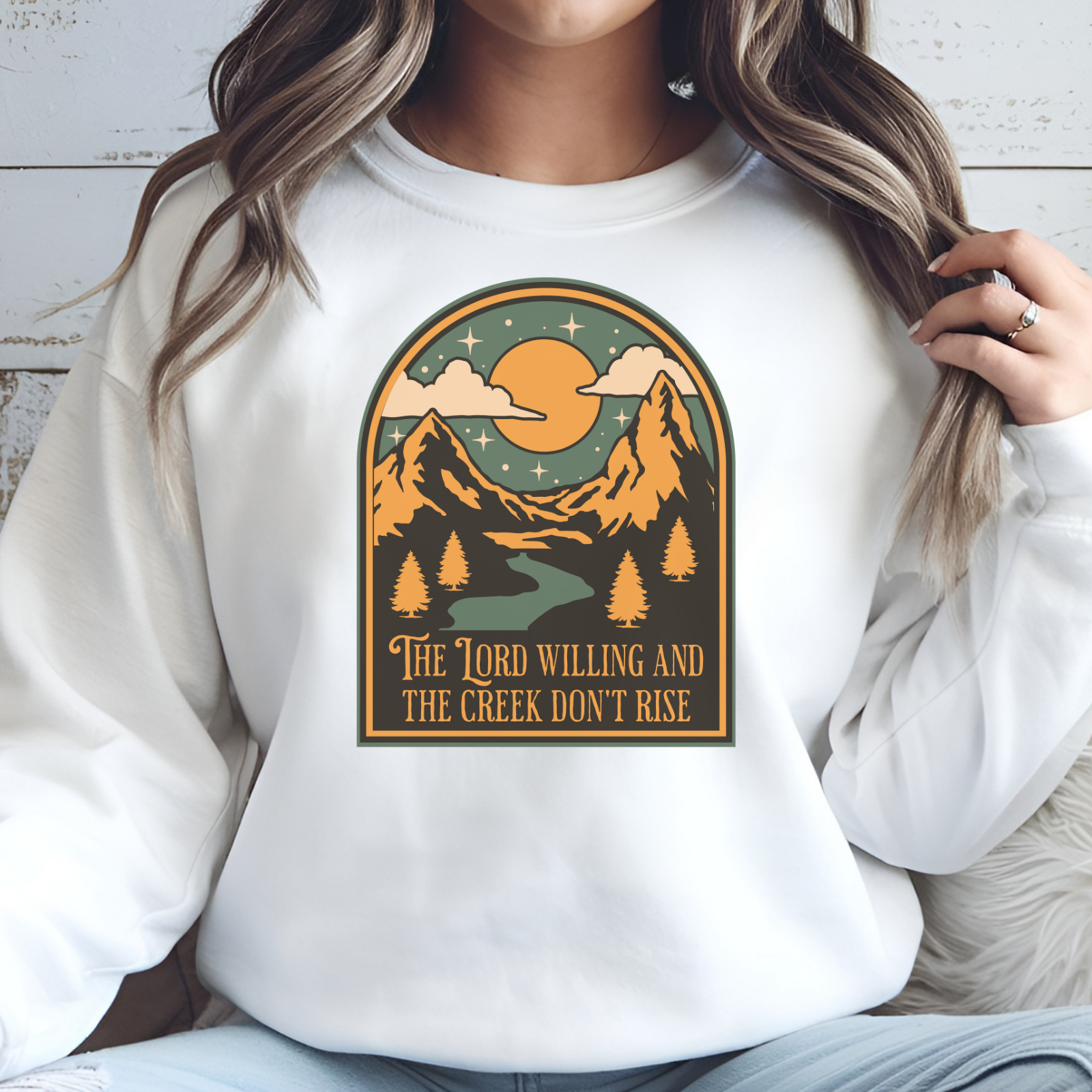 The Lord Willing And The Creek Don't Rise digital design on a woman's white sweatshirt