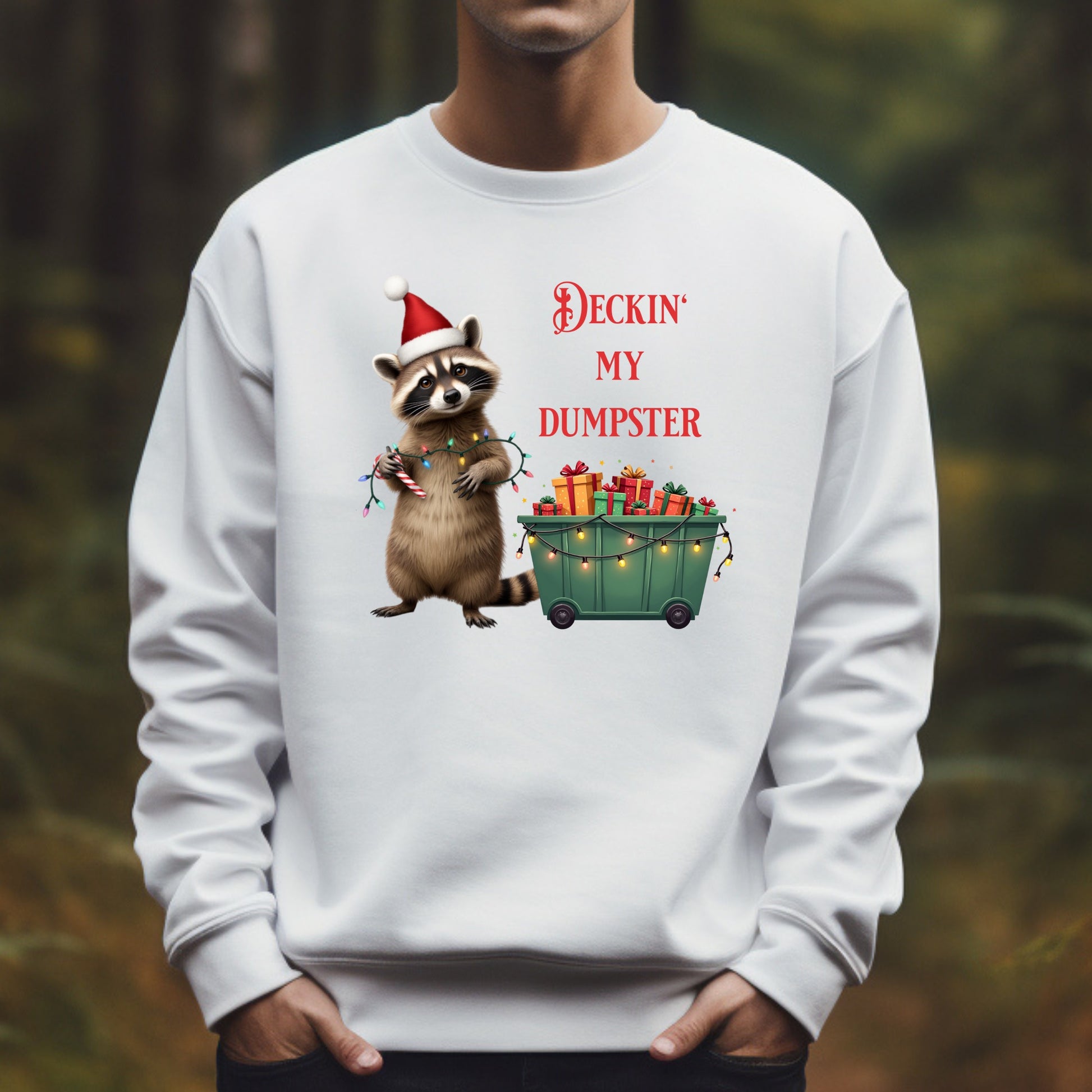 White sweatshirt with a Christmas-themed design of a raccoon and text, worn by a person outdoors.