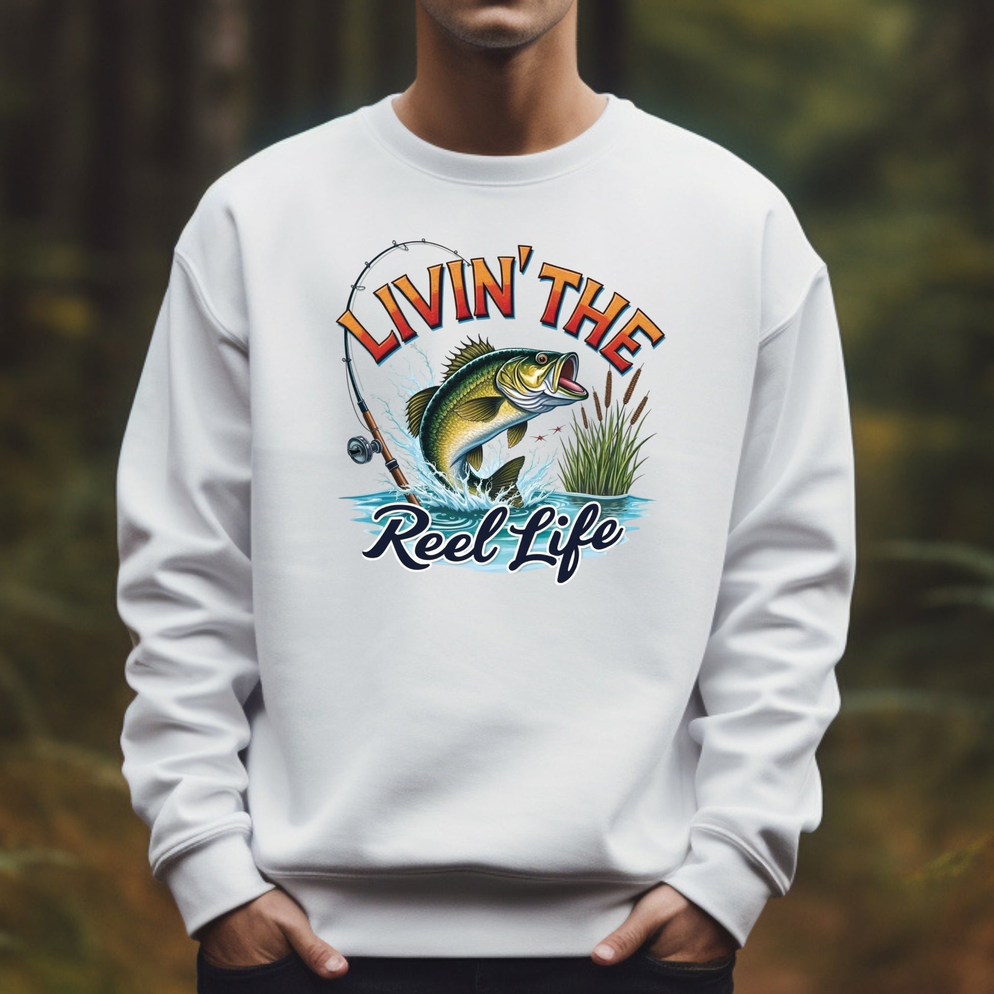 Man wearing a white sweatshirt with a fishing graphic and text 'Livin' The Reel Life' against a blurred natural background.