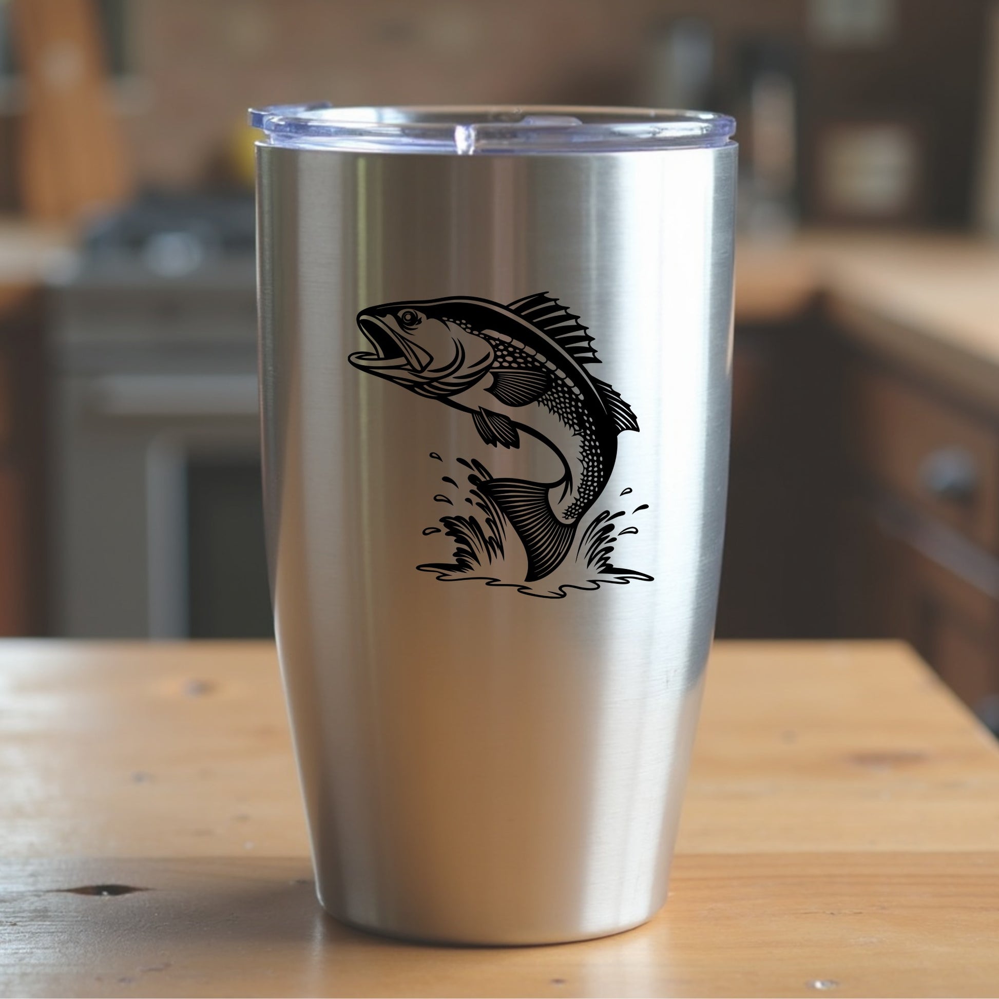 Silver tumbler with a walleye fish design on a wooden surface in a kitchen setting