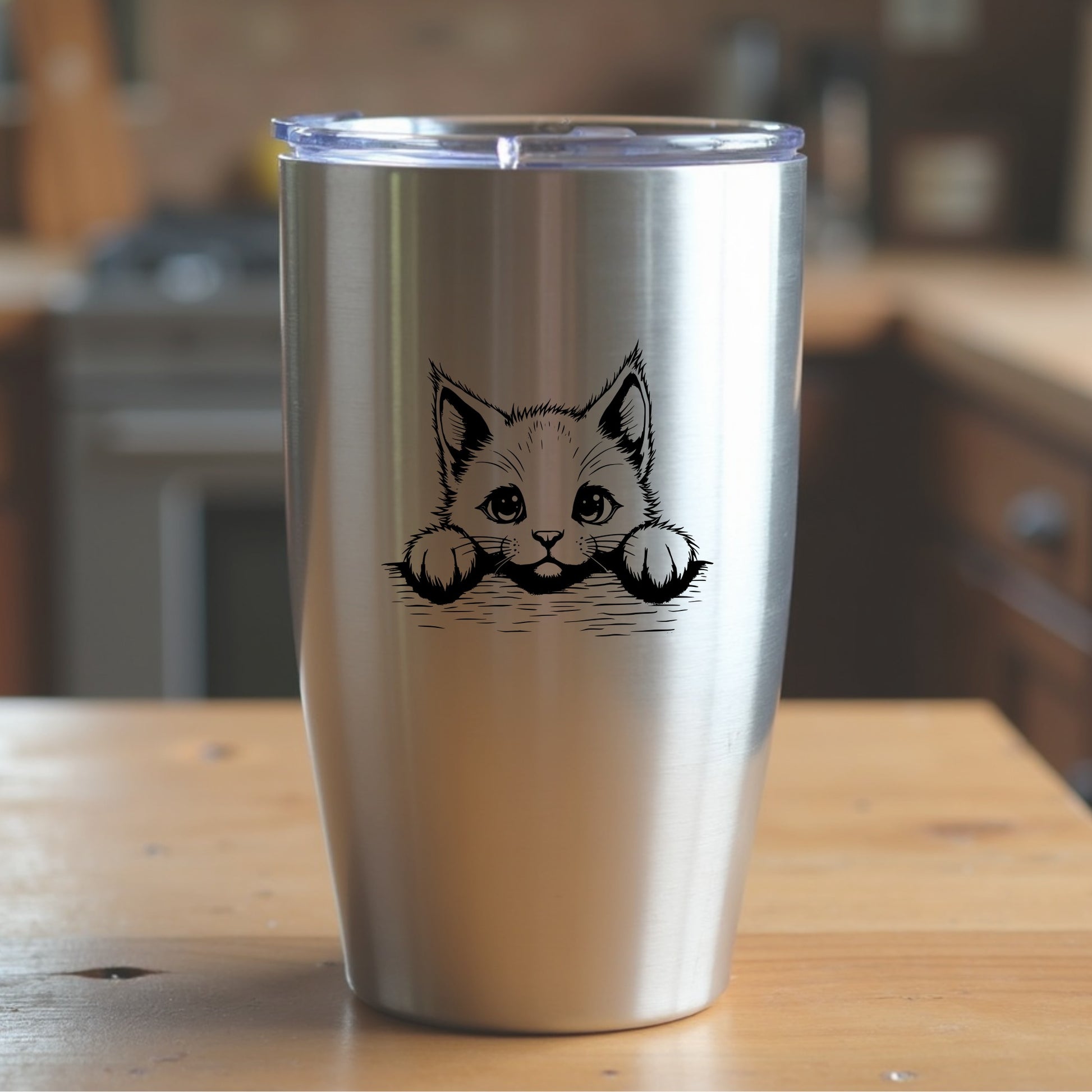 Silver tumbler with a cat design on a wooden surface in a kitchen setting