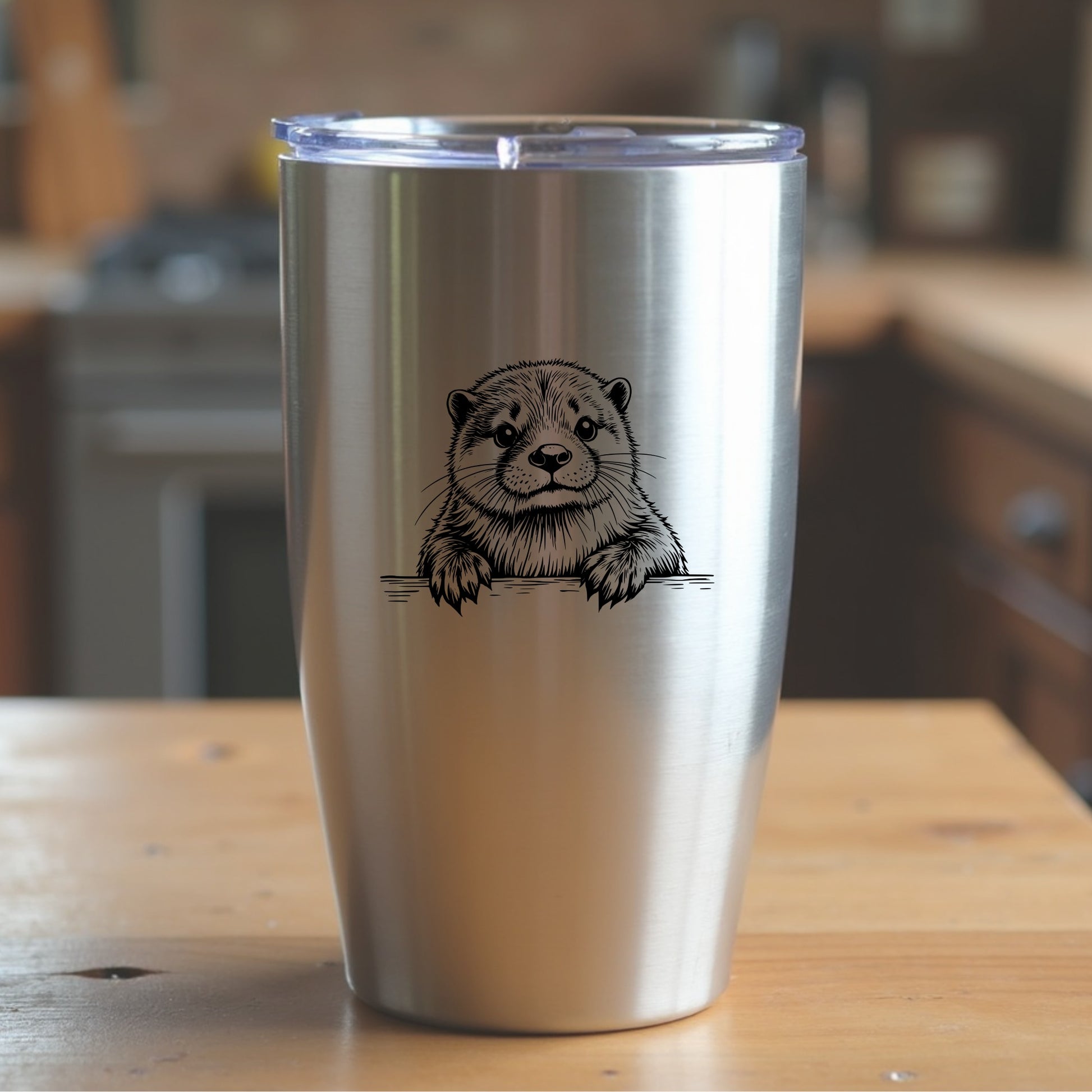 Silver tumbler with an otter design on a wooden surface in a kitchen setting