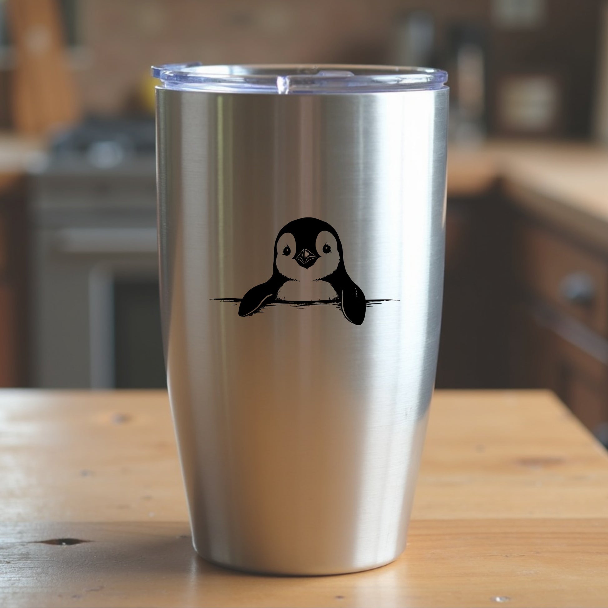 Silver tumbler with a penguin design on a wooden surface in a kitchen setting