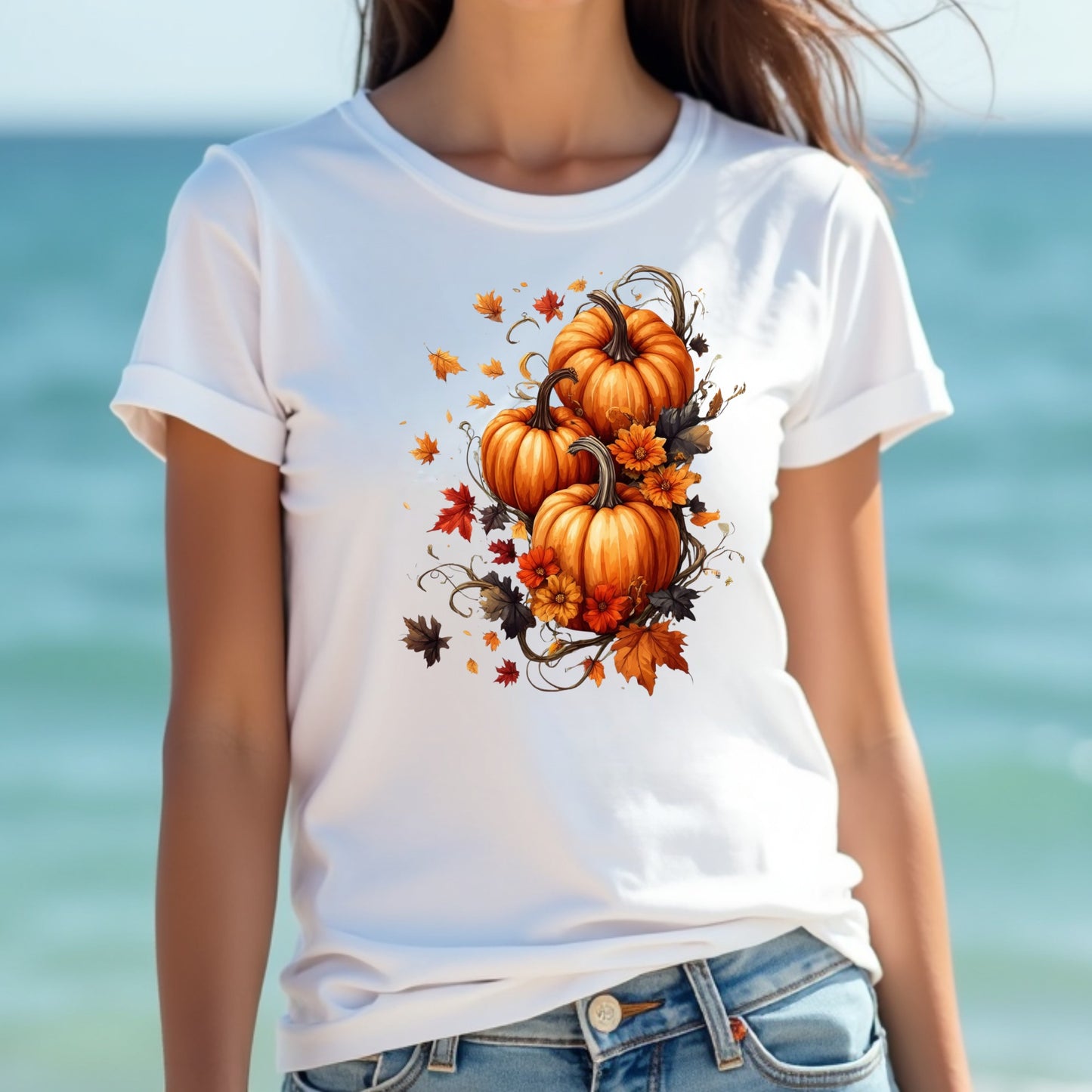Woman wearing a white t-shirt with pumpkins and leaves design by the ocean.
