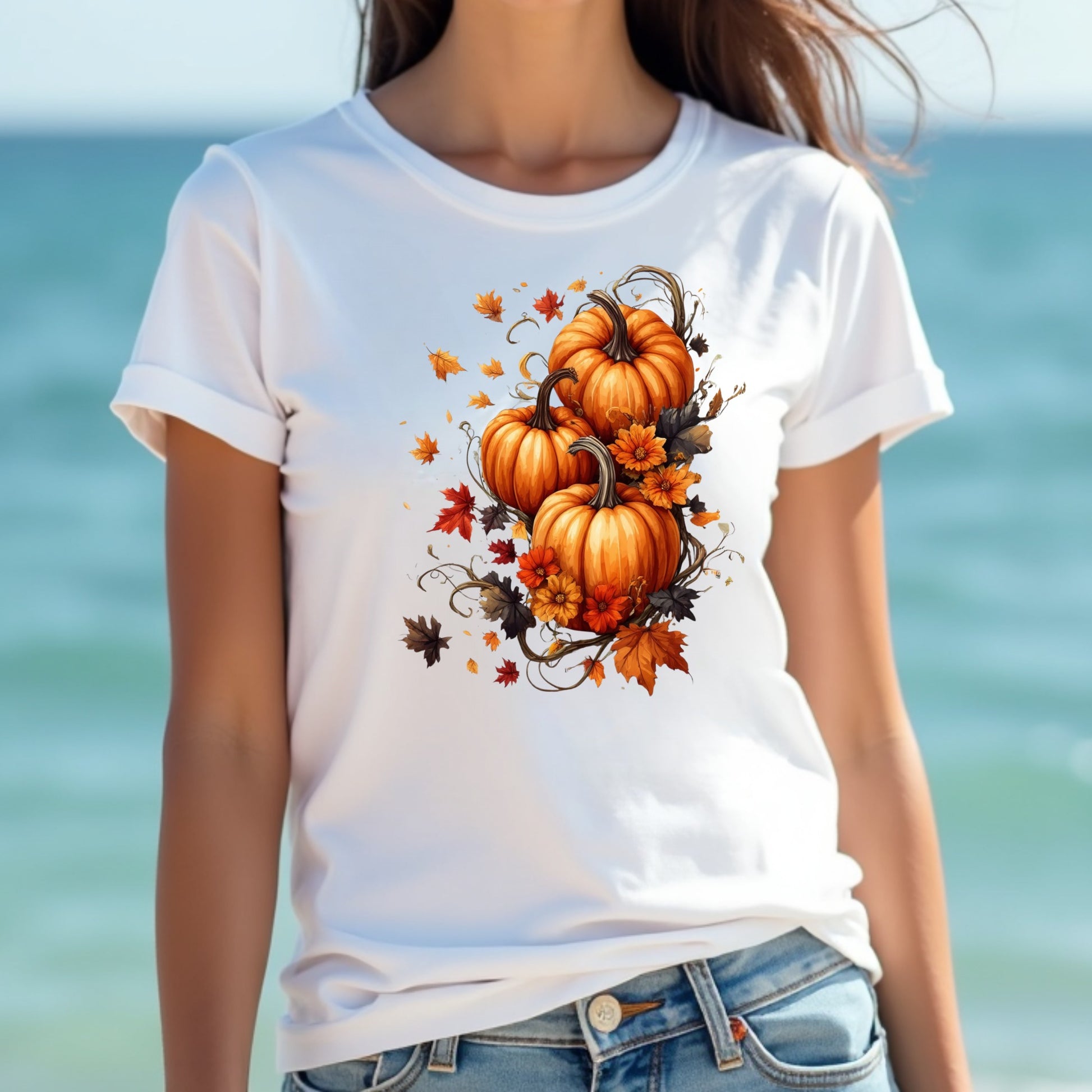Woman wearing a white t-shirt with pumpkins and leaves design by the ocean.