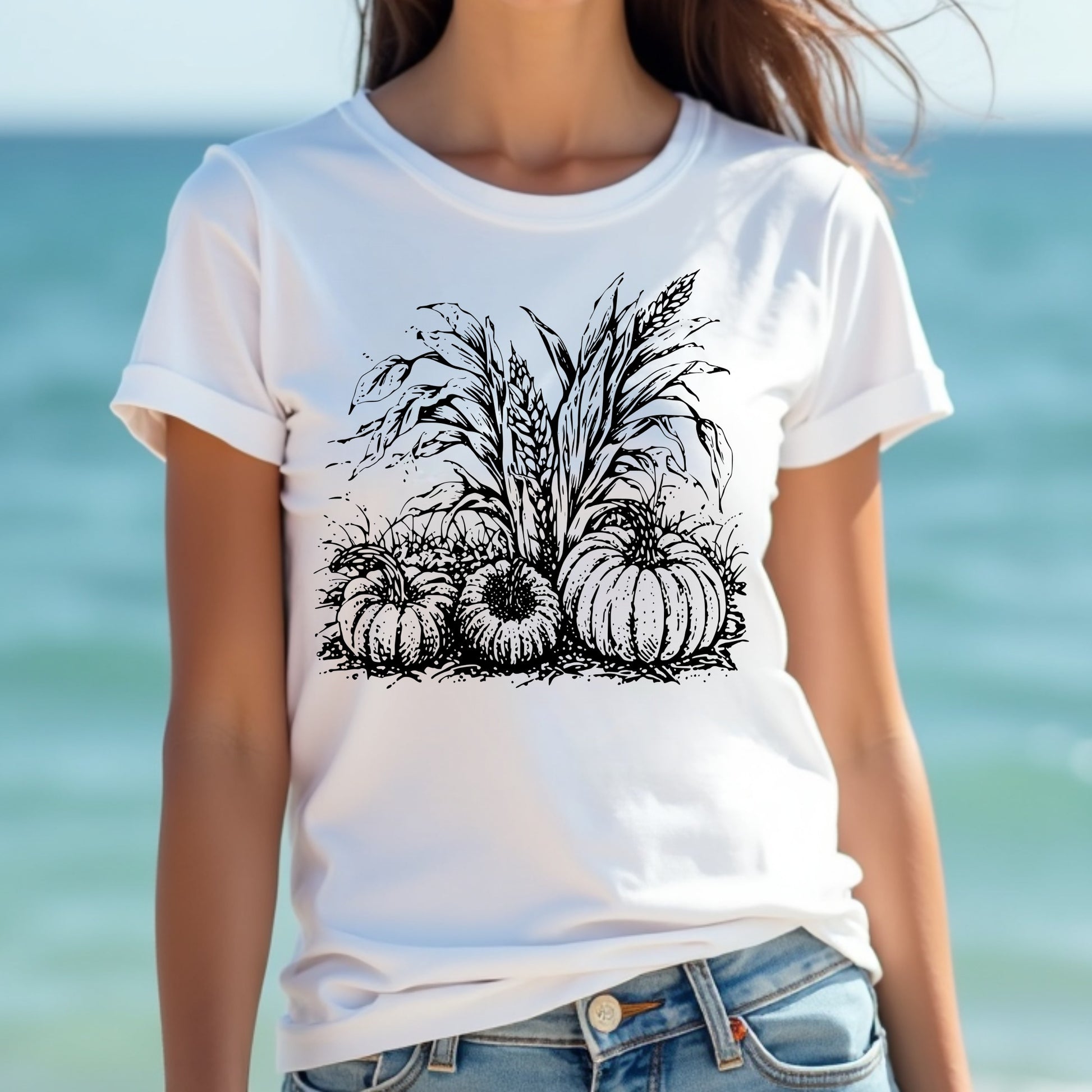 Woman wearing a white t-shirt with black pumpkin and corn design against a blurred ocean background