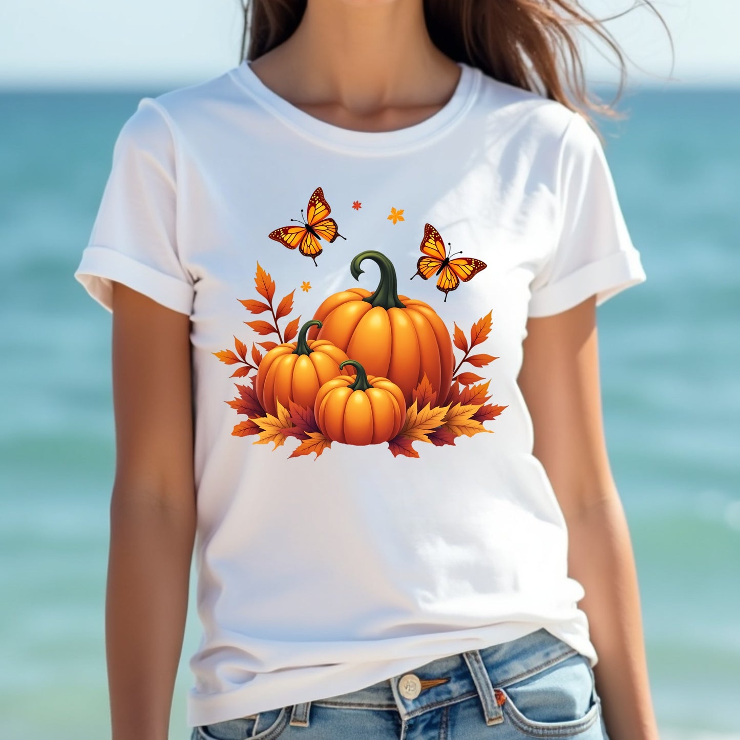 Woman wearing a white t-shirt with pumpkins and butterflies design against a blurred beach background
