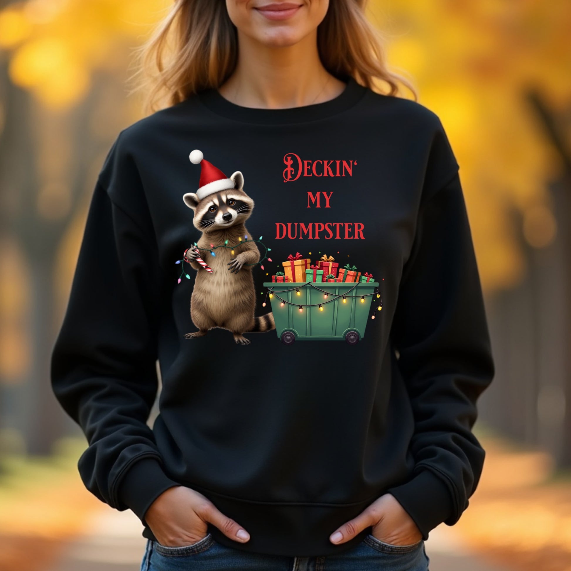 Woman wearing a black sweatshirt with a Christmas-themed raccoon graphic in an autumn setting.