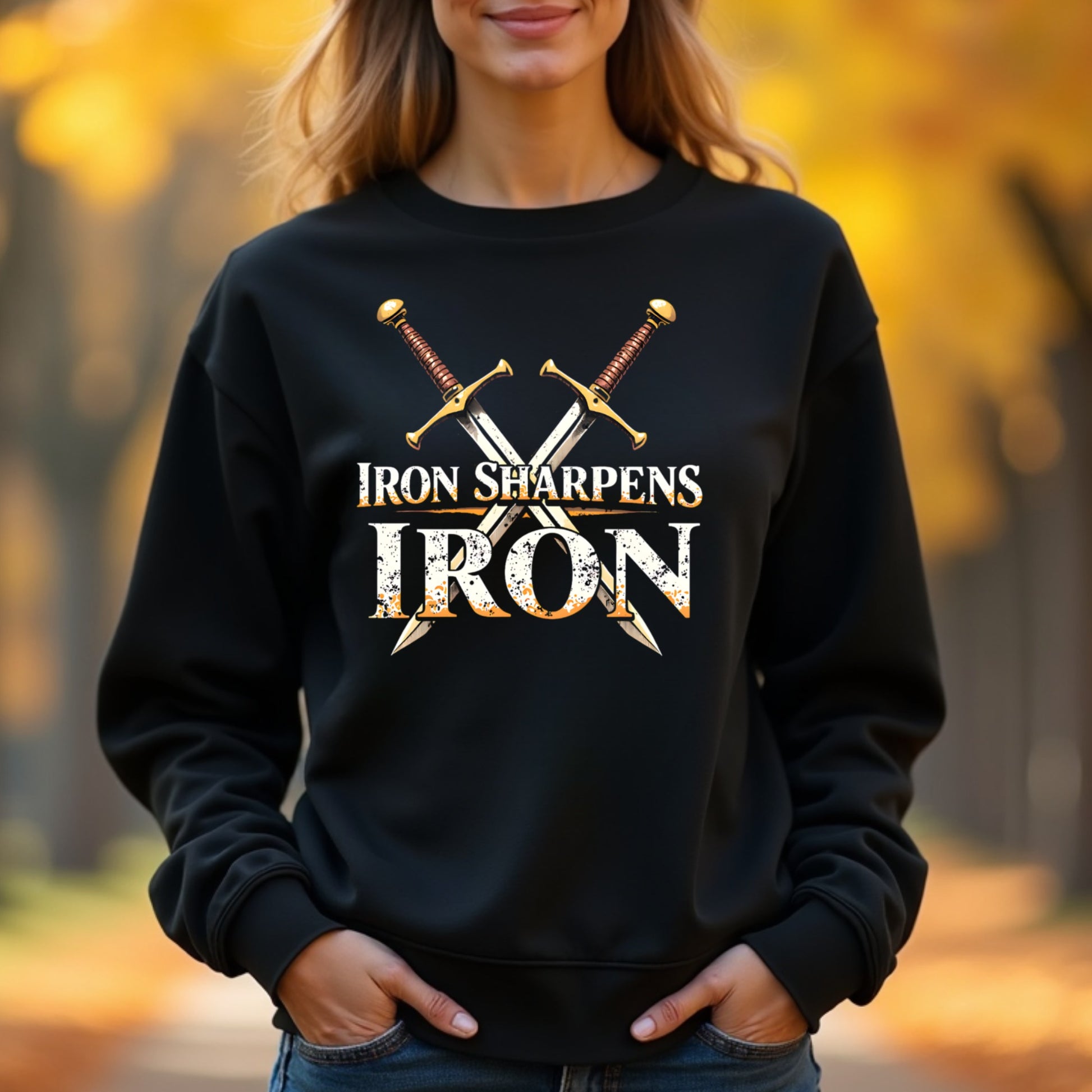 Woman wearing a black sweatshirt with 'Iron Sharpens Iron' text and crossed swords design outdoors.