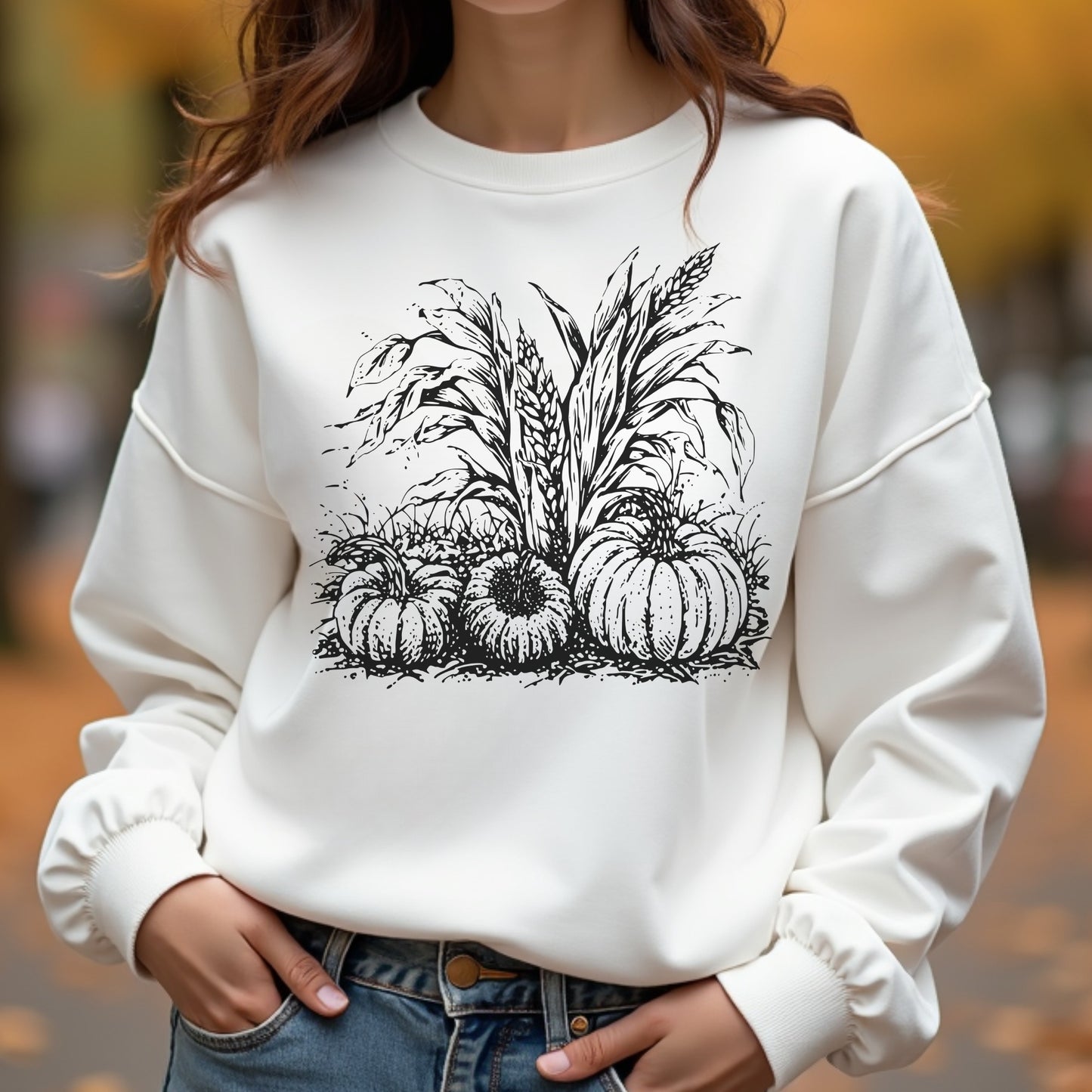 White sweatshirt with black pumpkin and corn design worn by a woman outdoors.
