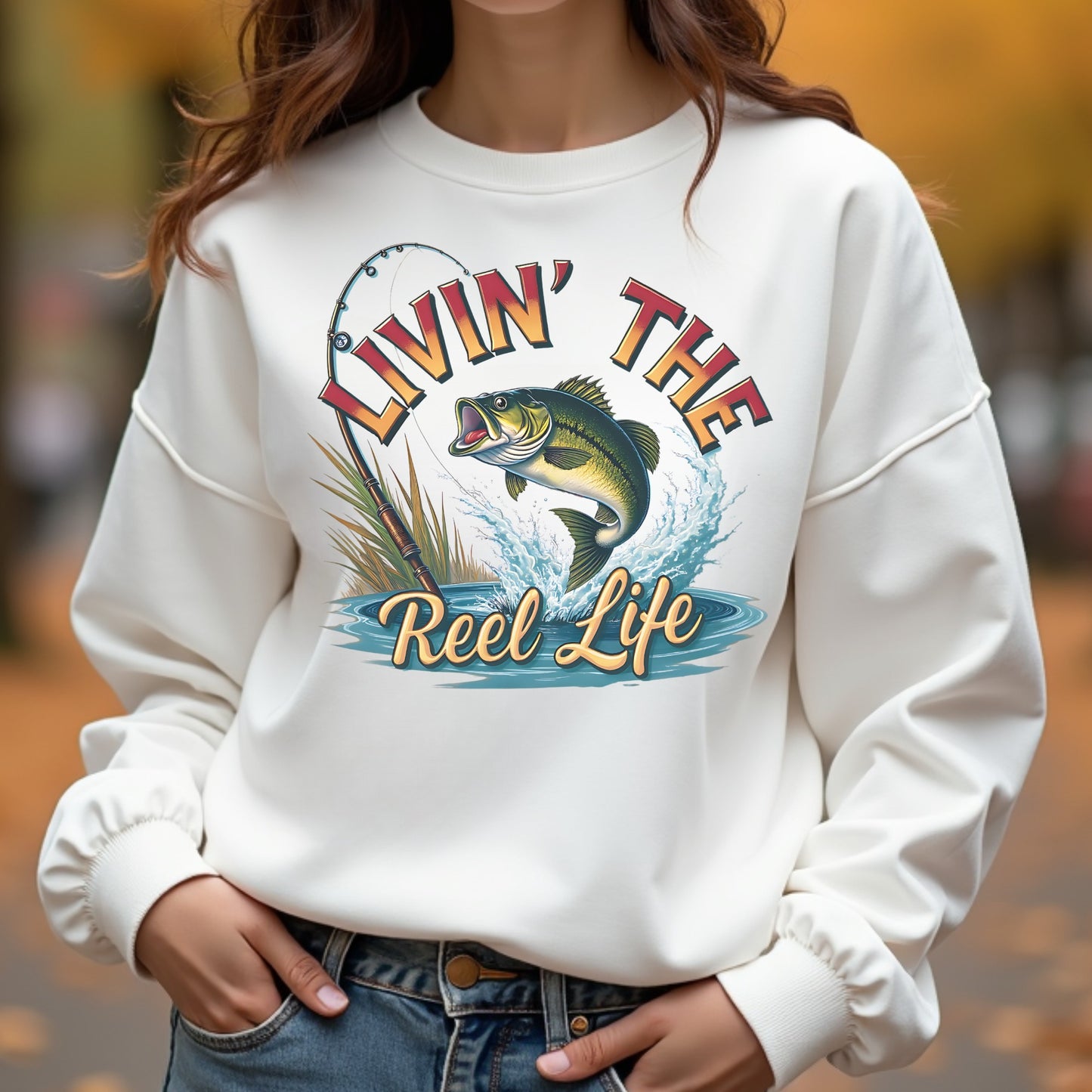 Woman wearing a white sweatshirt with a fishing graphic and text 'Livin' The Reel Life'.