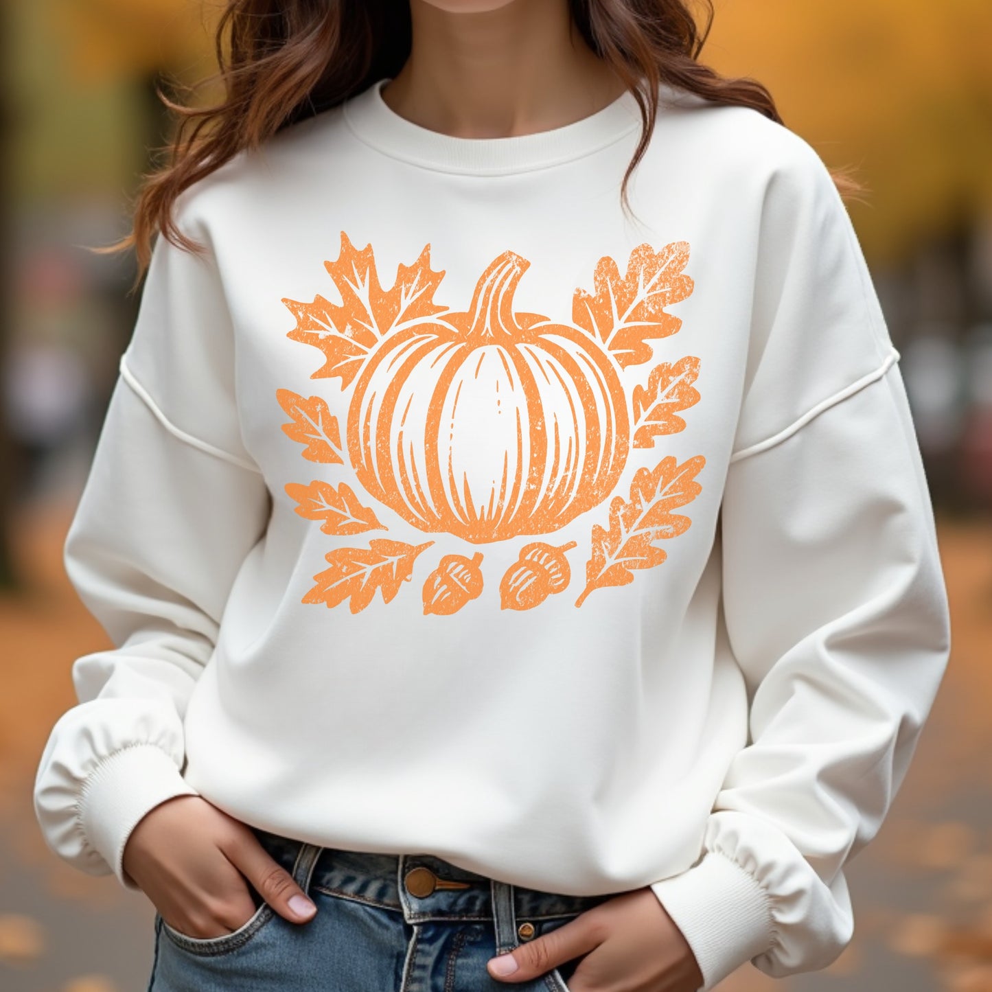 White sweatshirt with orange pumpkin design worn by a woman outdoors.