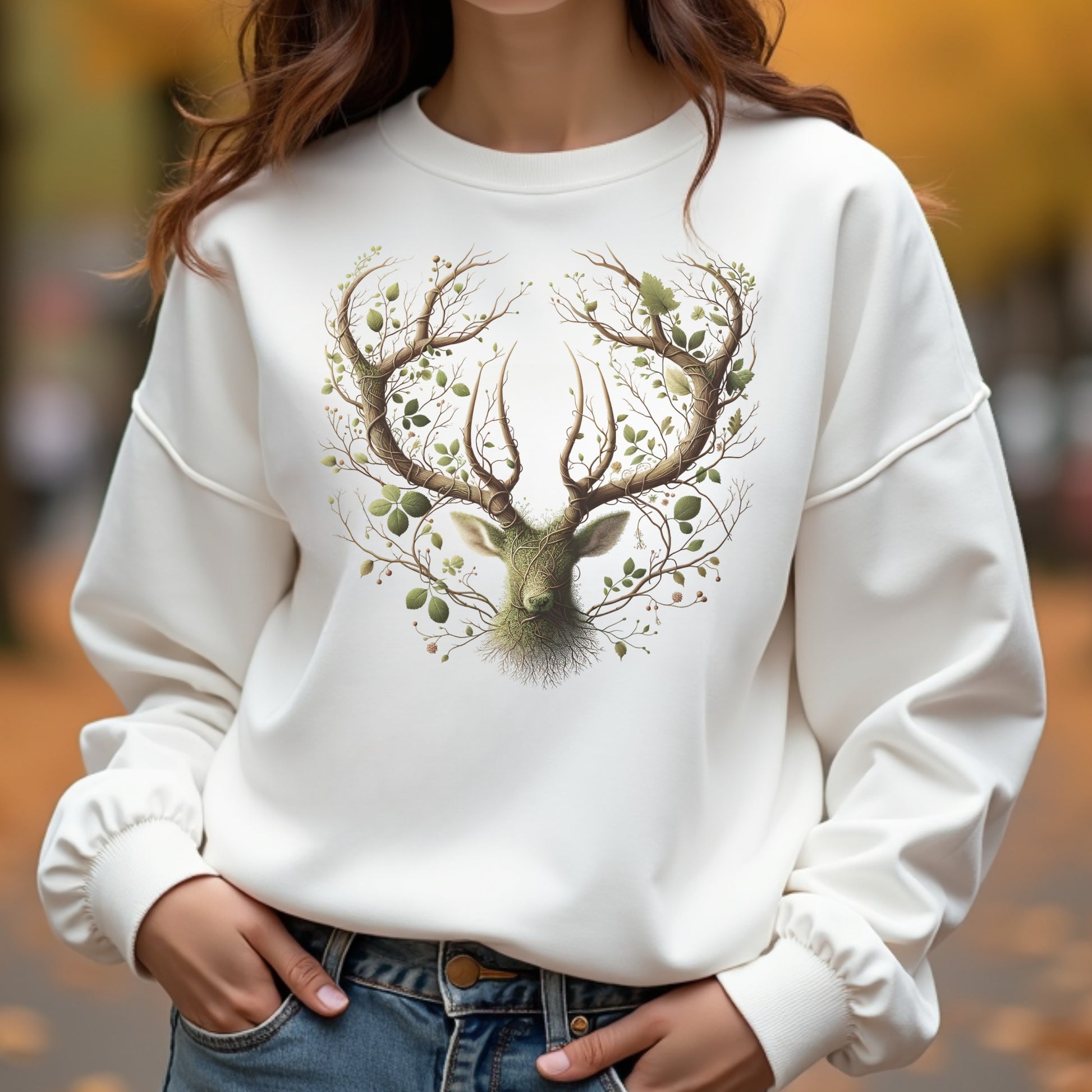 White sweatshirt with a deer and nature design worn by a woman outdoors.