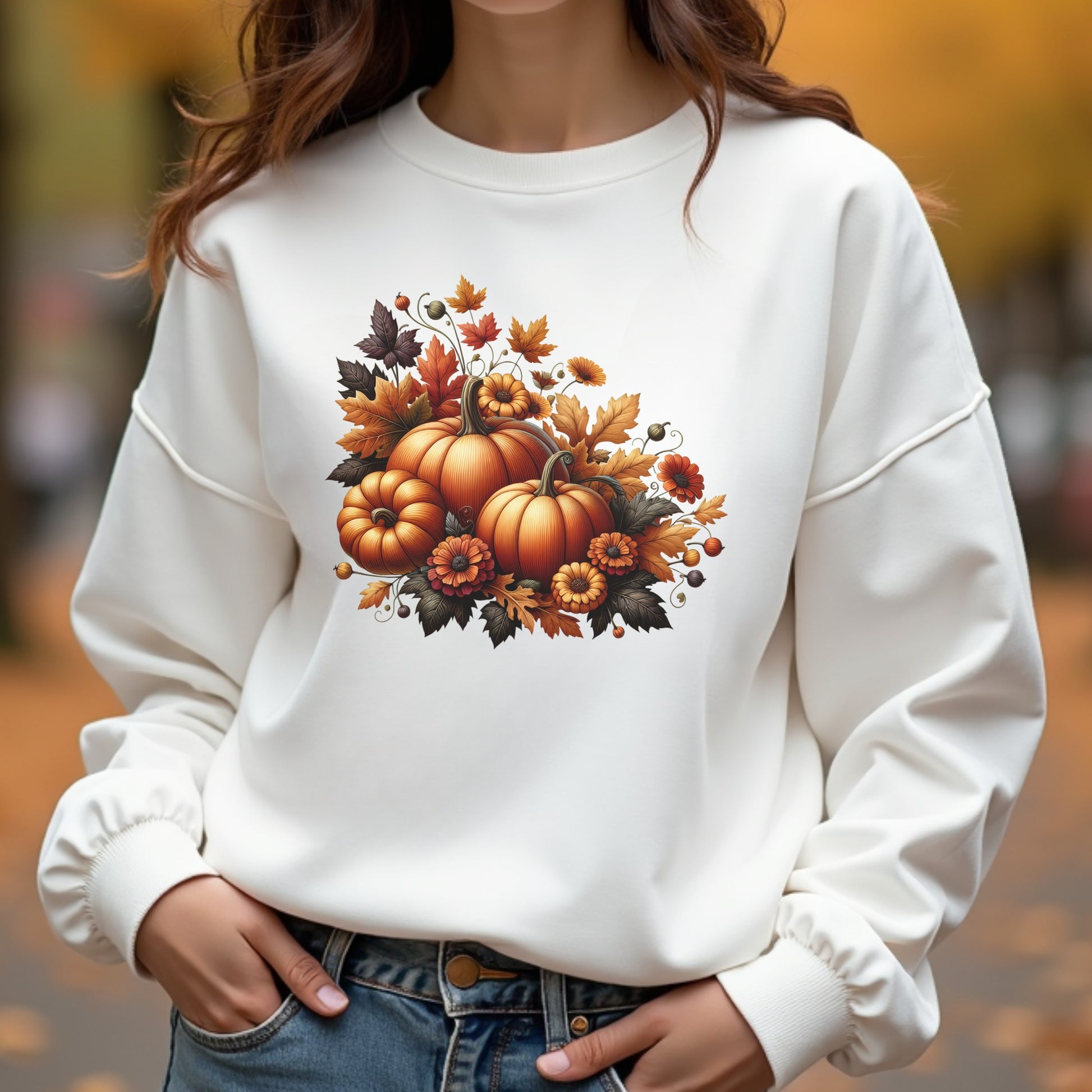 White sweatshirt with pumpkin and leaf design worn by a woman outdoors.