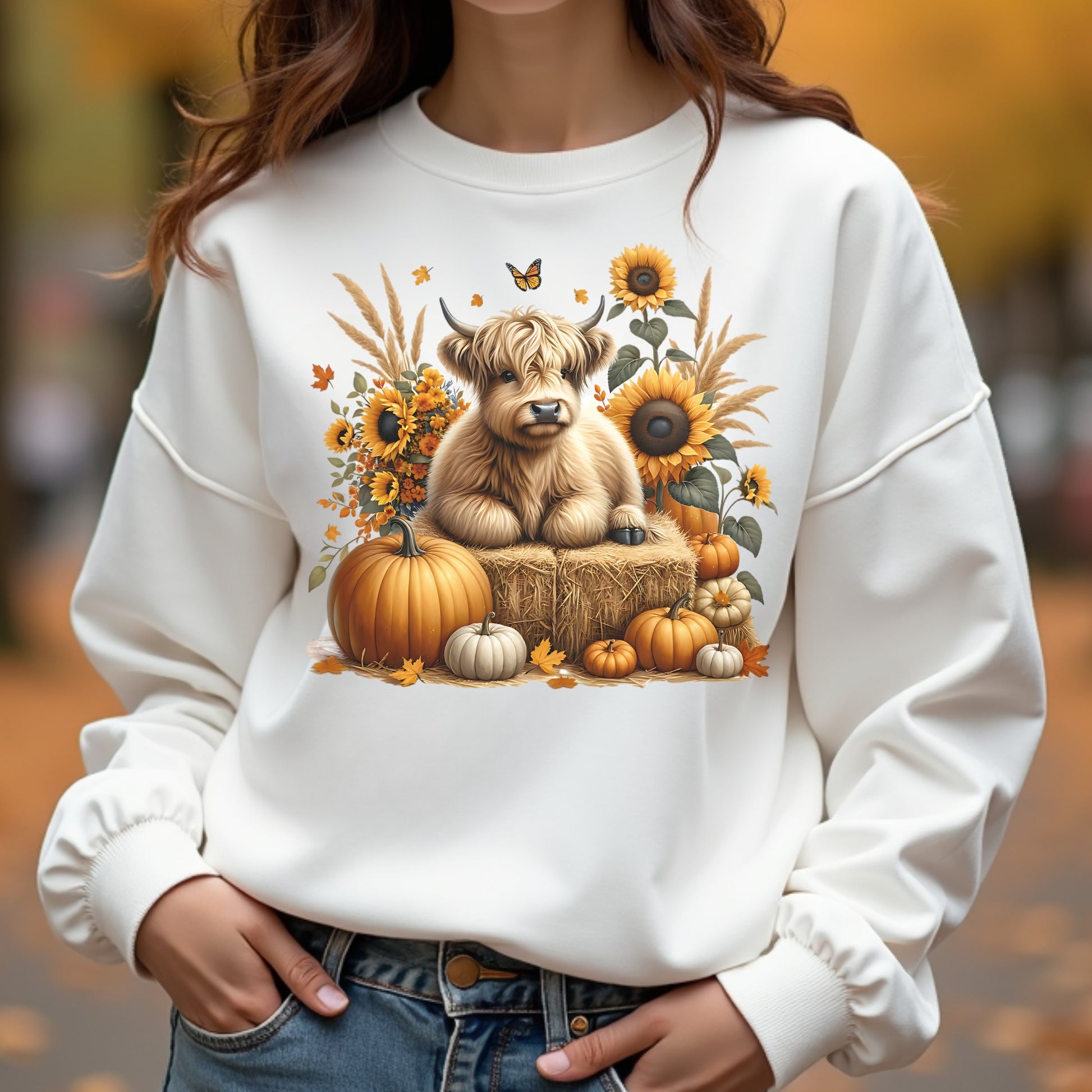 White sweatshirt with a Highland cow and autumn elements design, worn by a woman.
