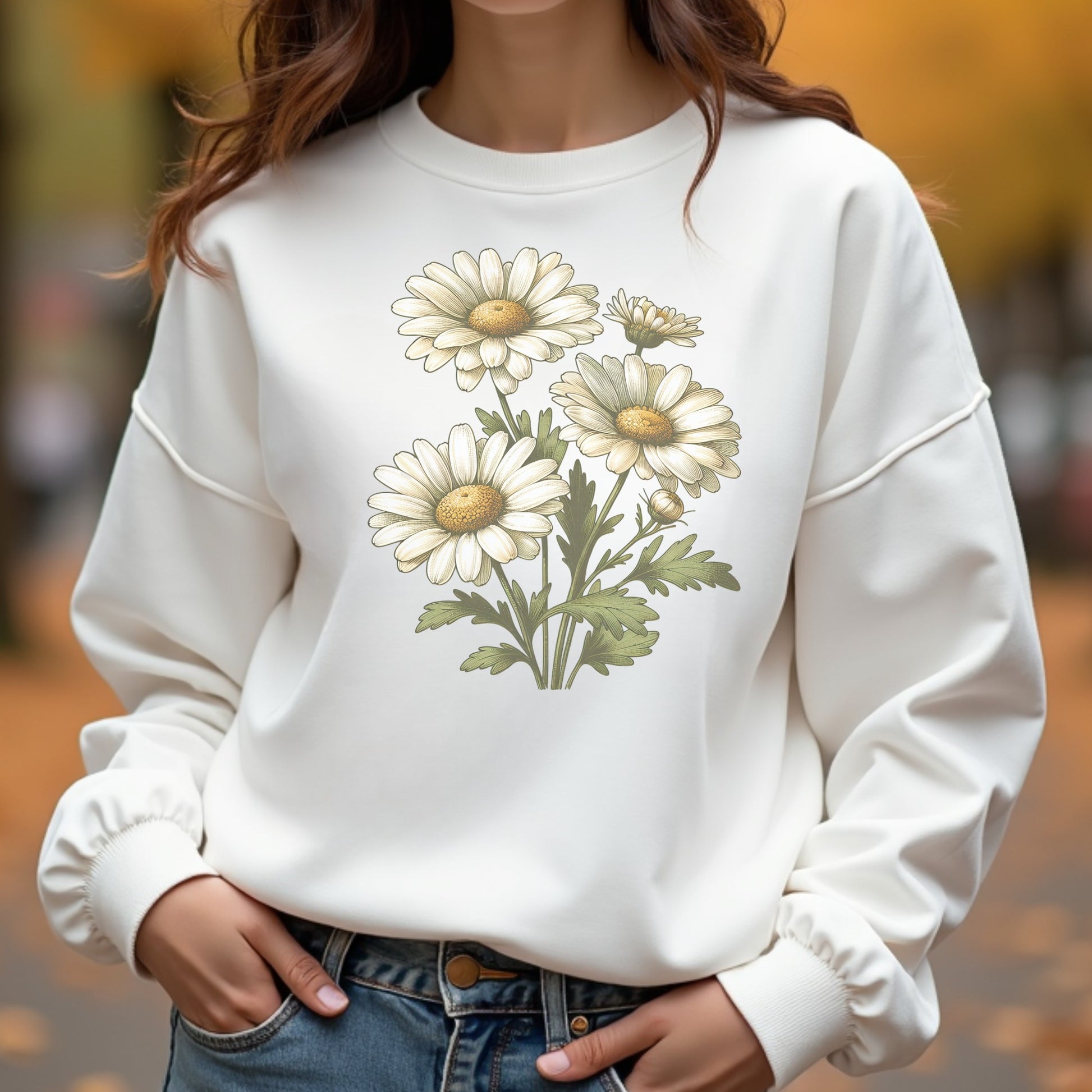White sweatshirt with daisy design worn by a woman, blurred outdoor background