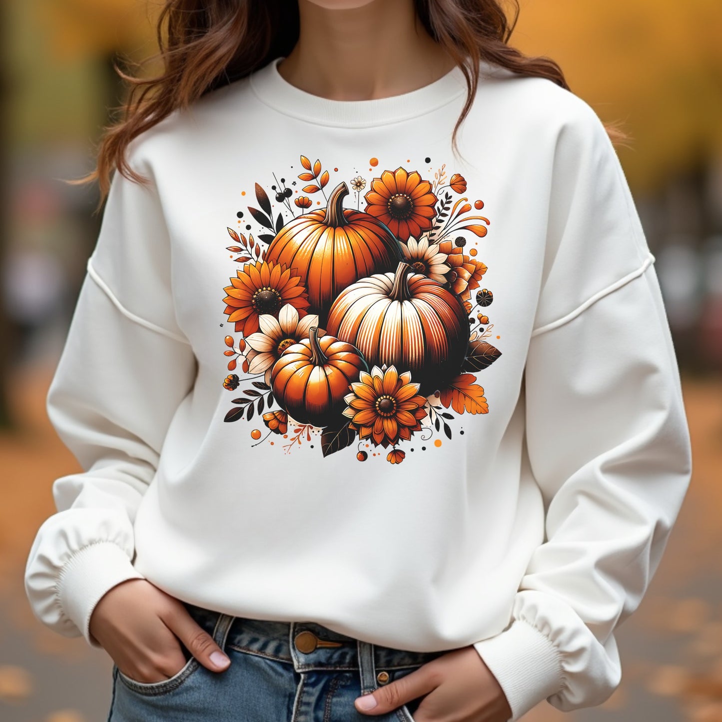 White sweatshirt with autumn-themed design featuring pumpkins and flowers, worn by a woman outdoors.
